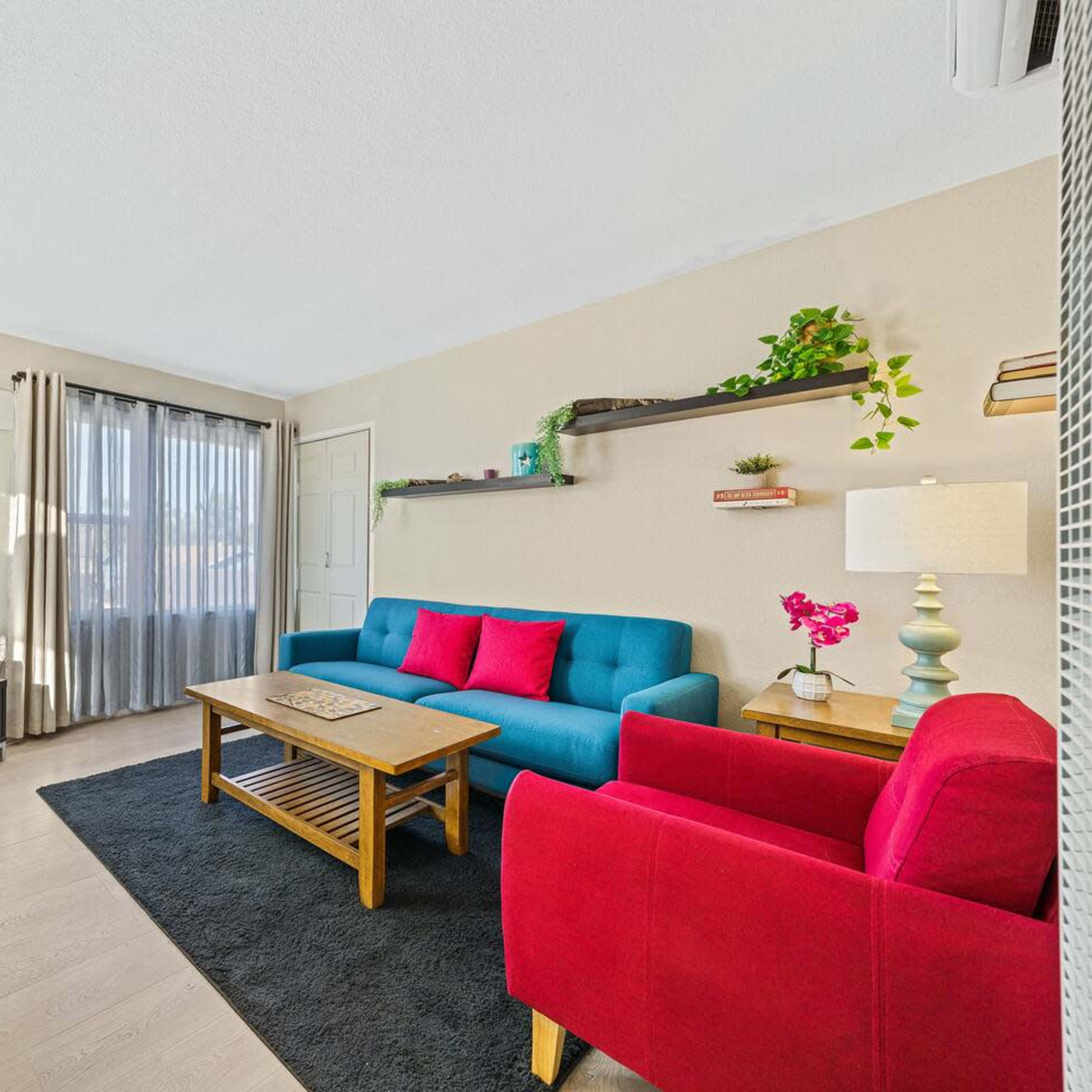 A modern living room featuring a blue sofa, a red armchair, a wooden coffee table, and a wall-mounted shelf with decorative items.