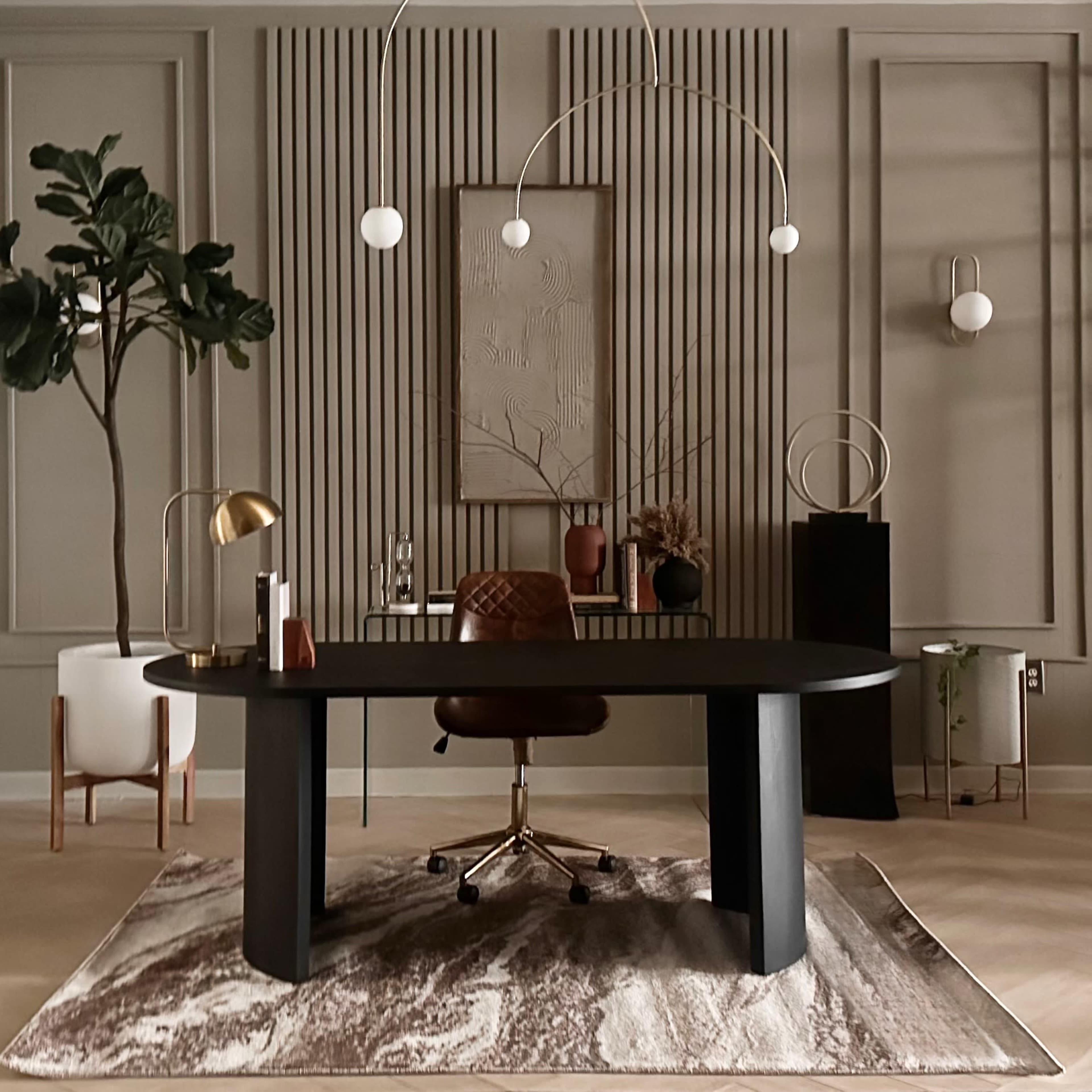 A modern office space features a round black desk with a brown office chair, surrounded by decorative plants and geometric wall panels.