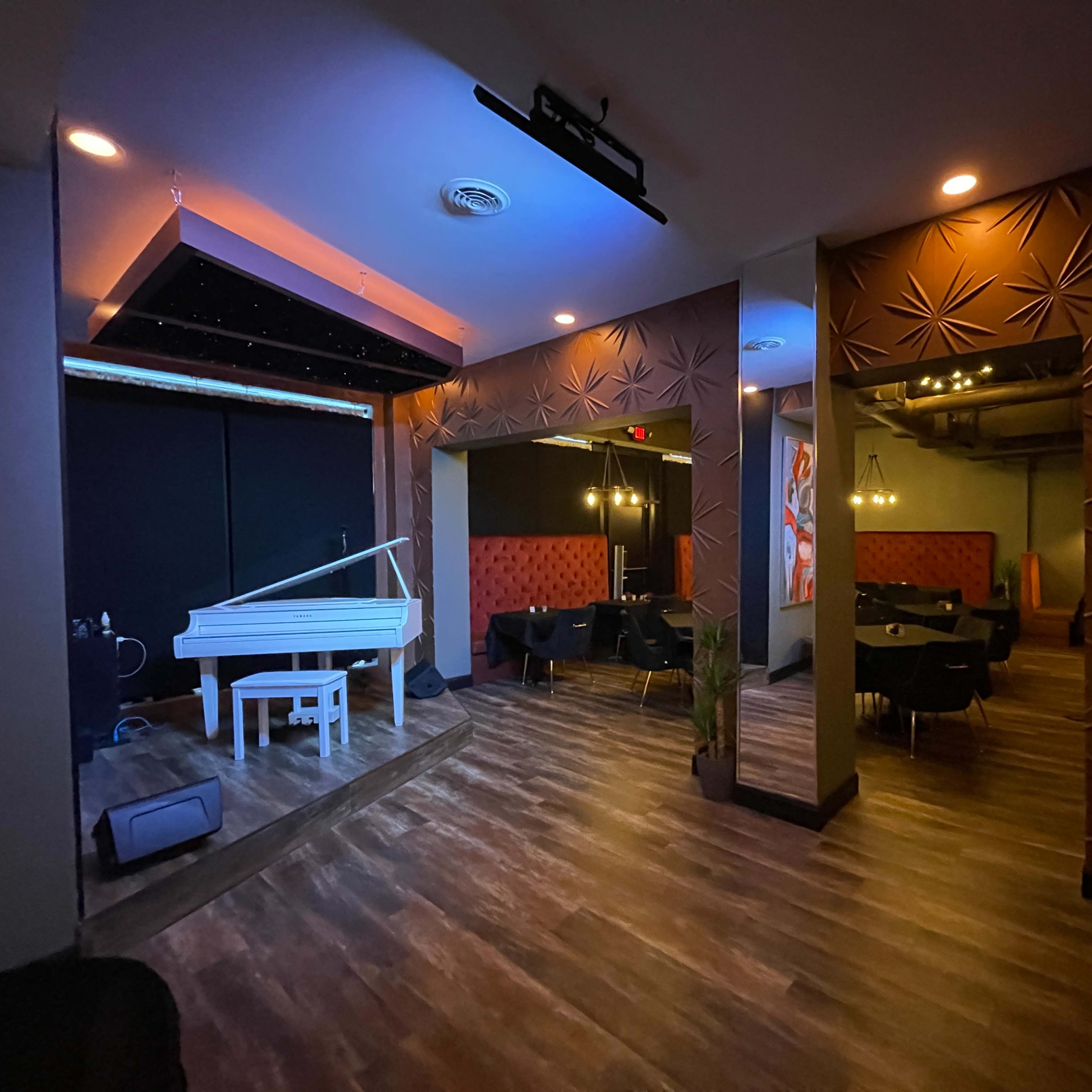 A dimly lit restaurant interior featuring a white grand piano, black tables, and decorative wall accents.
