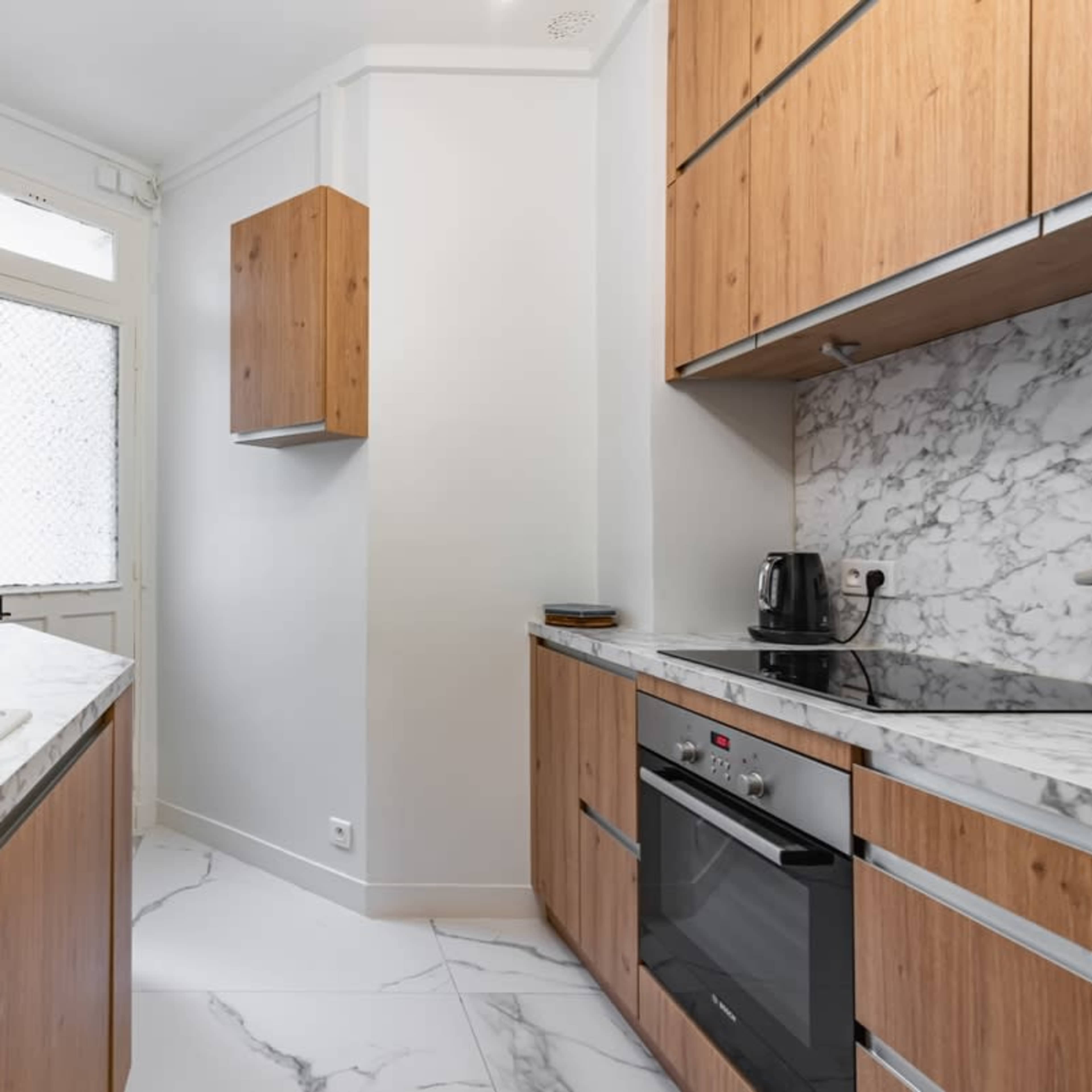 A modern kitchen features wooden cabinetry, marble countertops, and stainless steel appliances, with a window providing natural light.