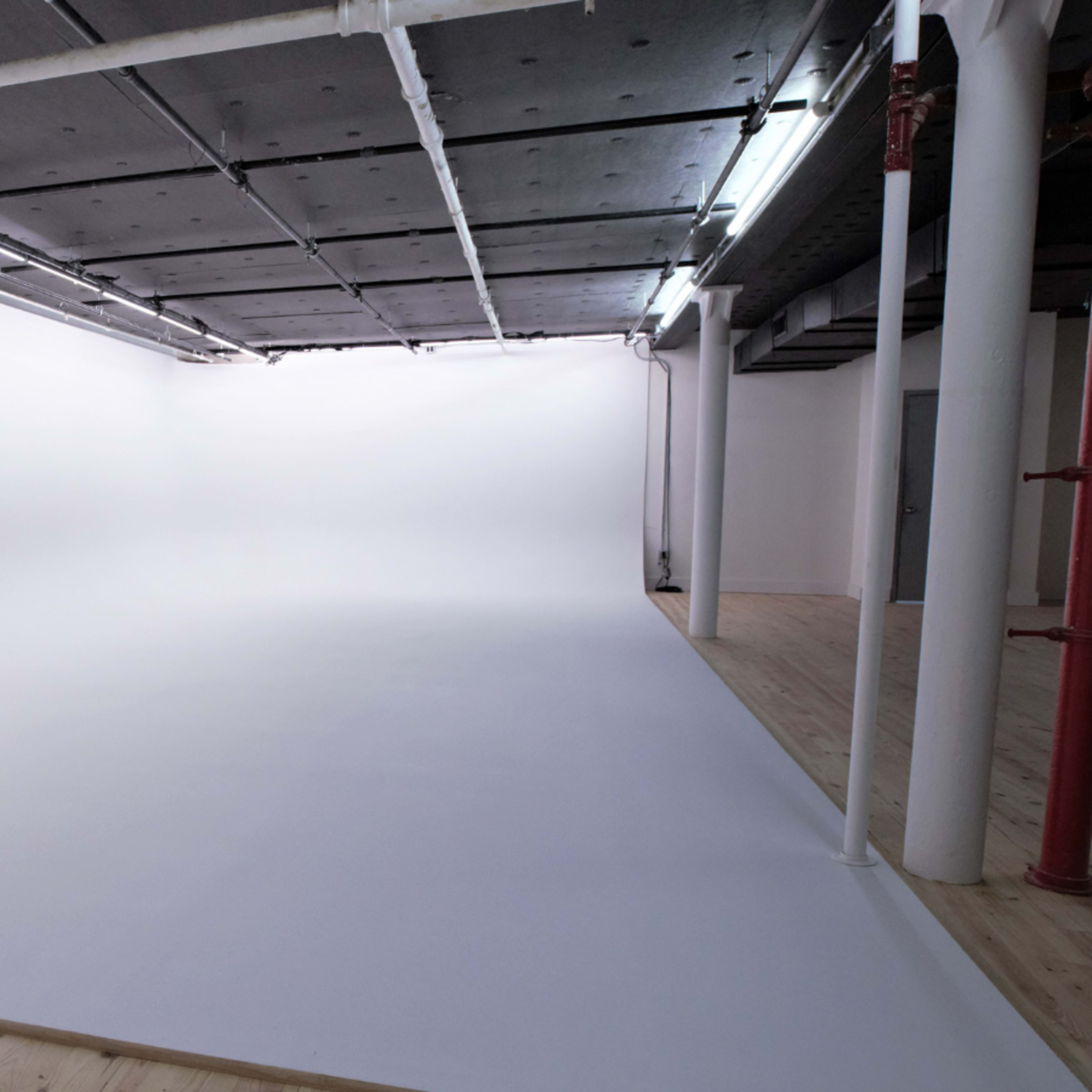 A spacious, empty photography studio with a seamless white backdrop and wooden flooring.