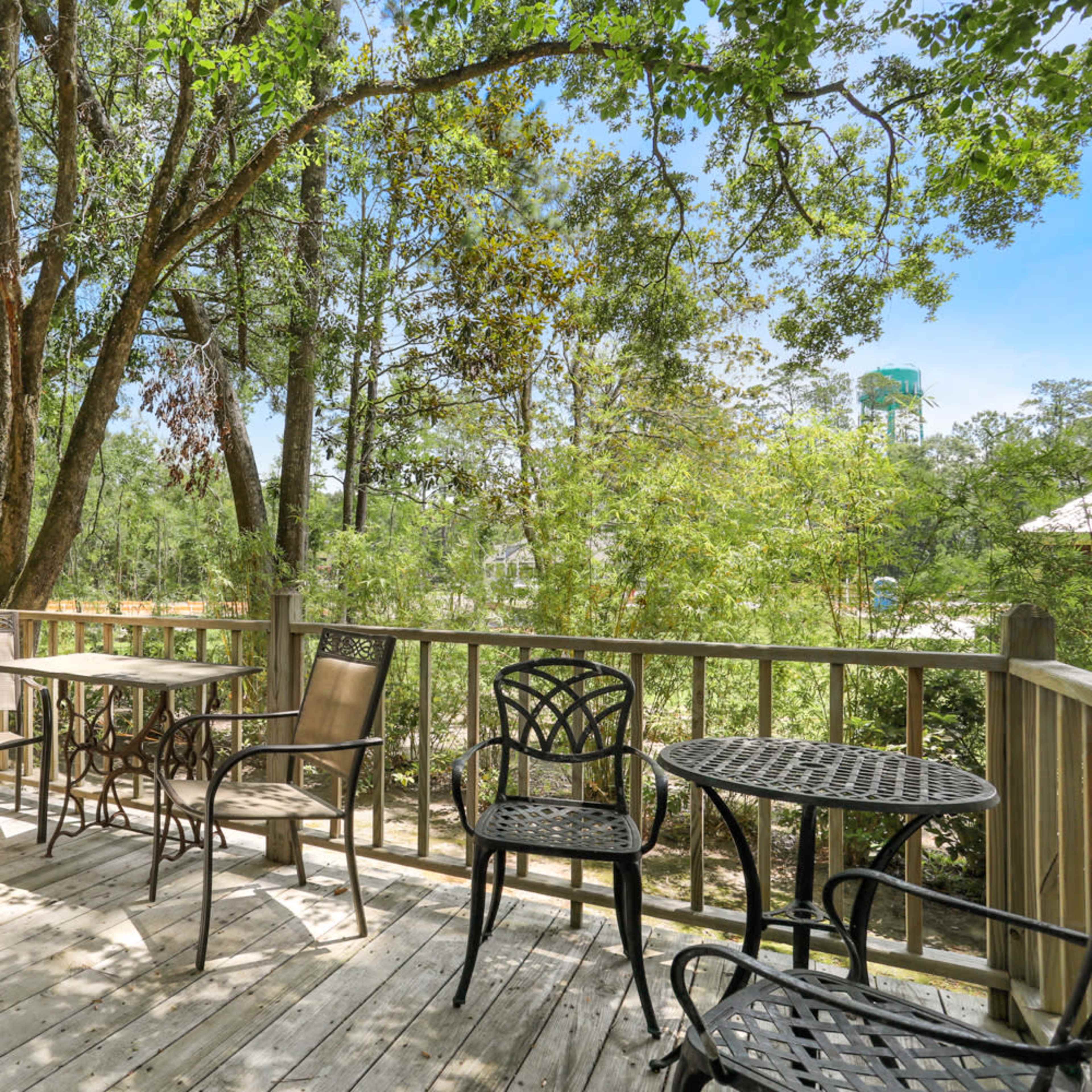 A wooden deck features several metal and wooden chairs and tables surrounded by trees.