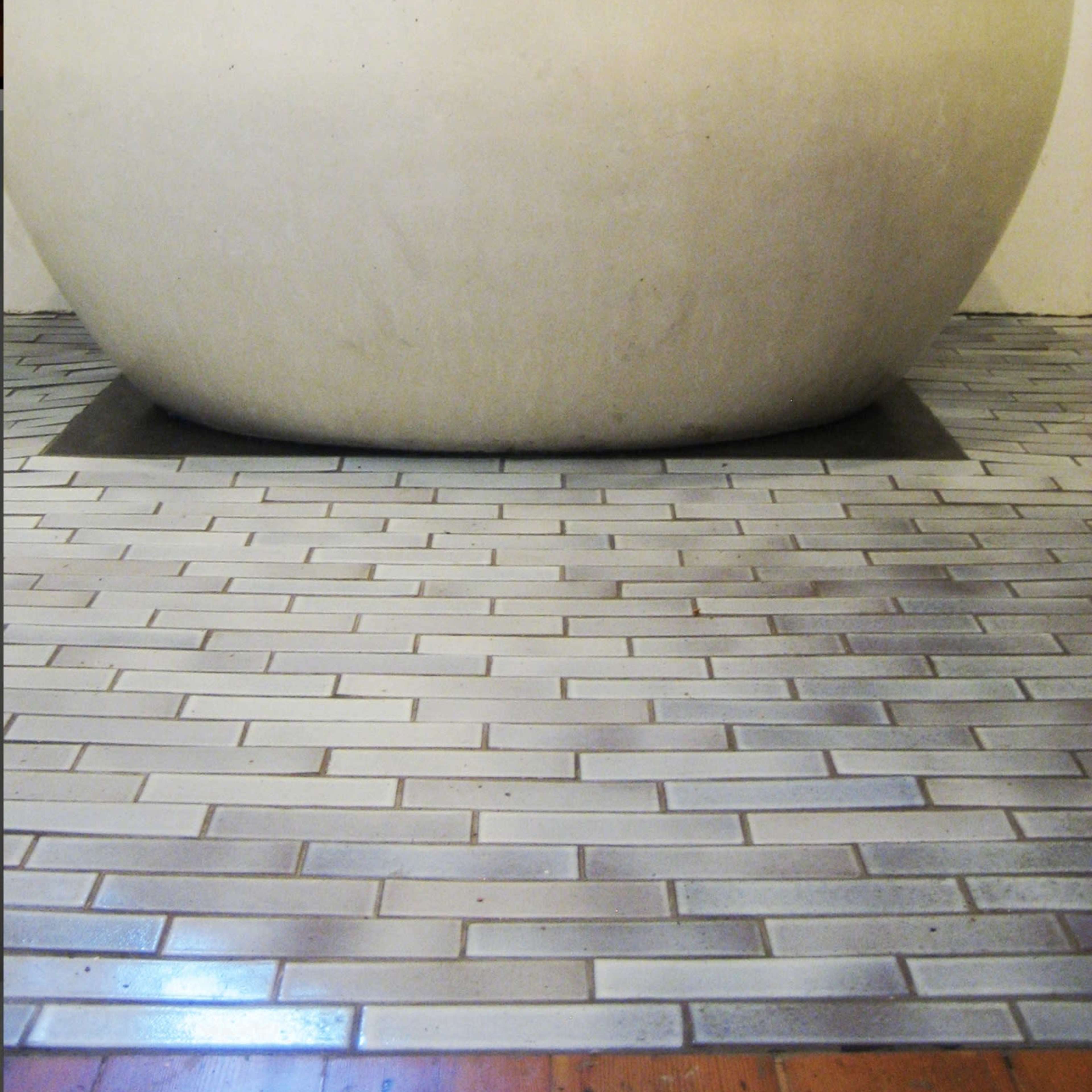 A round, smooth bathtub set on a floor composed of rectangular gray tiles.