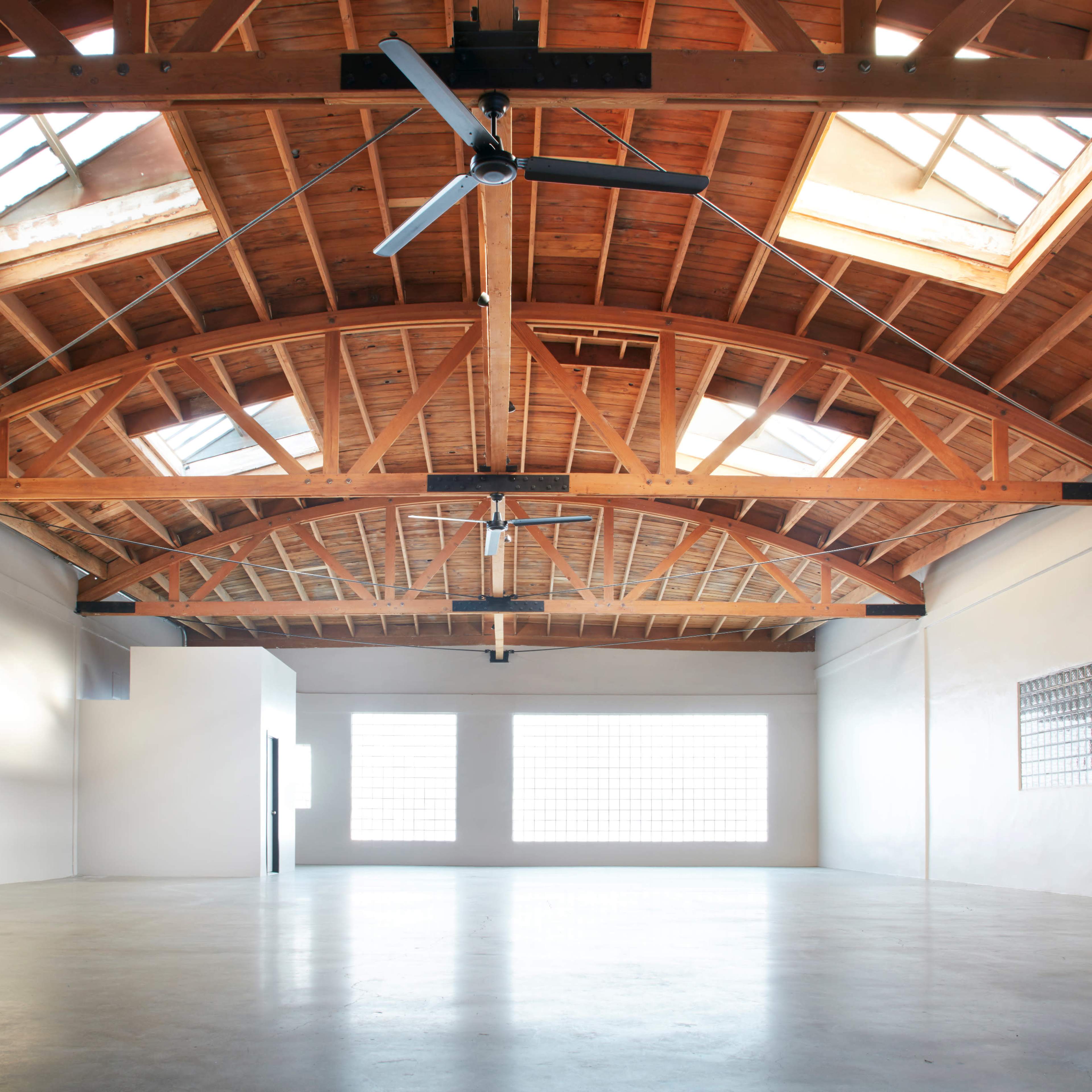 A spacious, empty room with a high wooden ceiling and large windows allowing natural light.