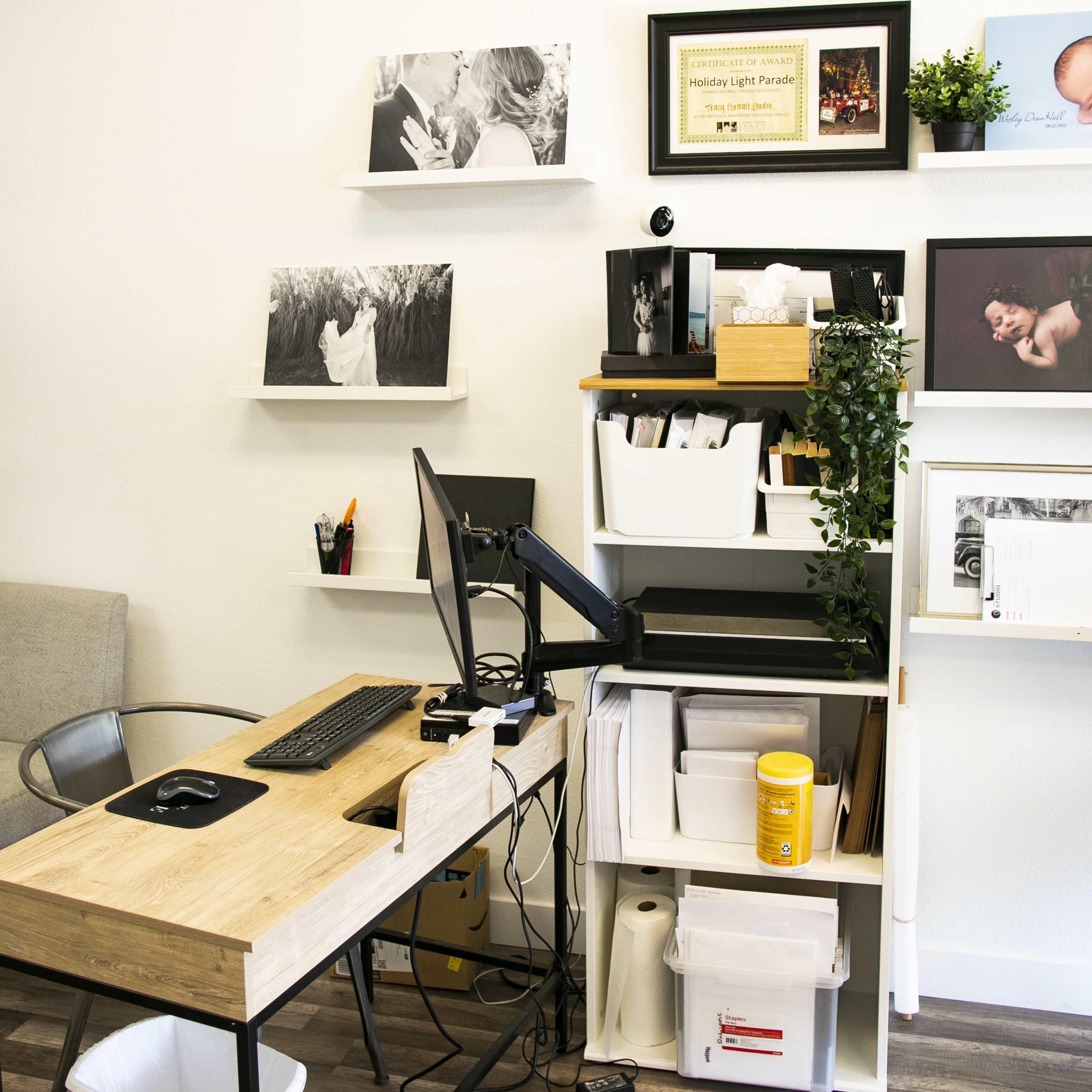 A small office space featuring a wooden desk with a computer, shelves displaying framed photographs, and storage units filled with boxes and documents.