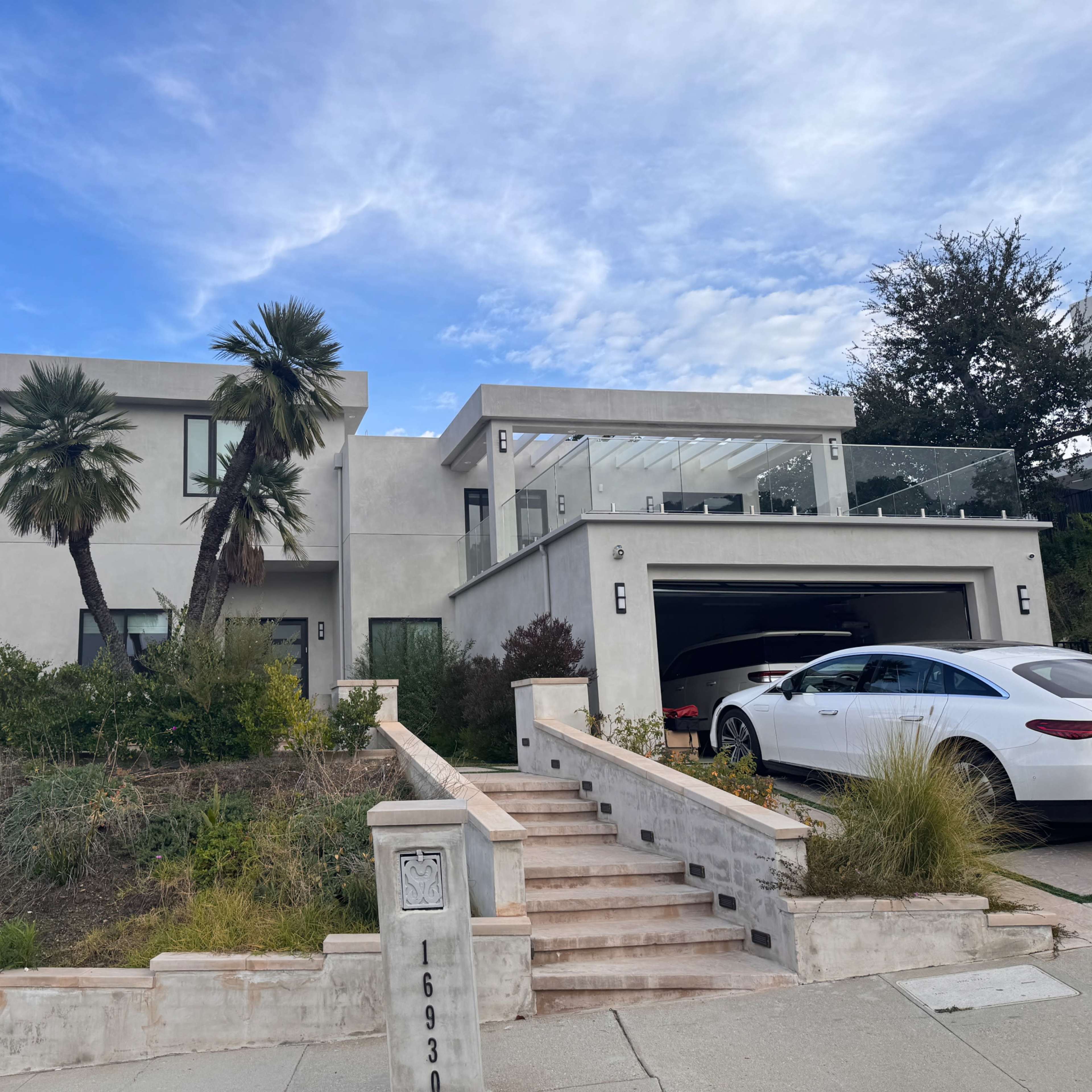 A modern two-story house with palm trees in the front yard and a driveway leading to a garage.