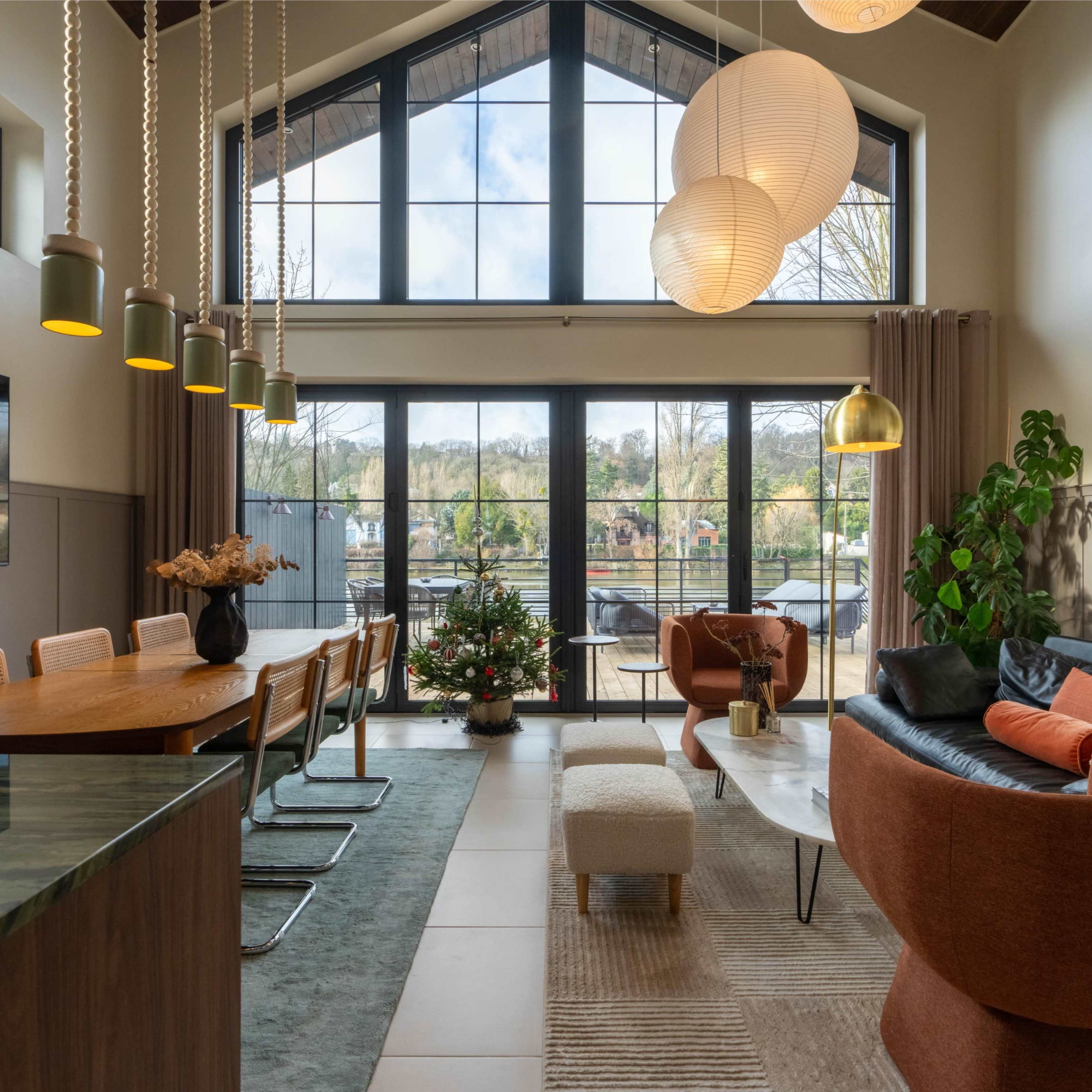 A modern living space with a large window view of a patio, featuring a dining table, comfortable seating, and decorative plants.