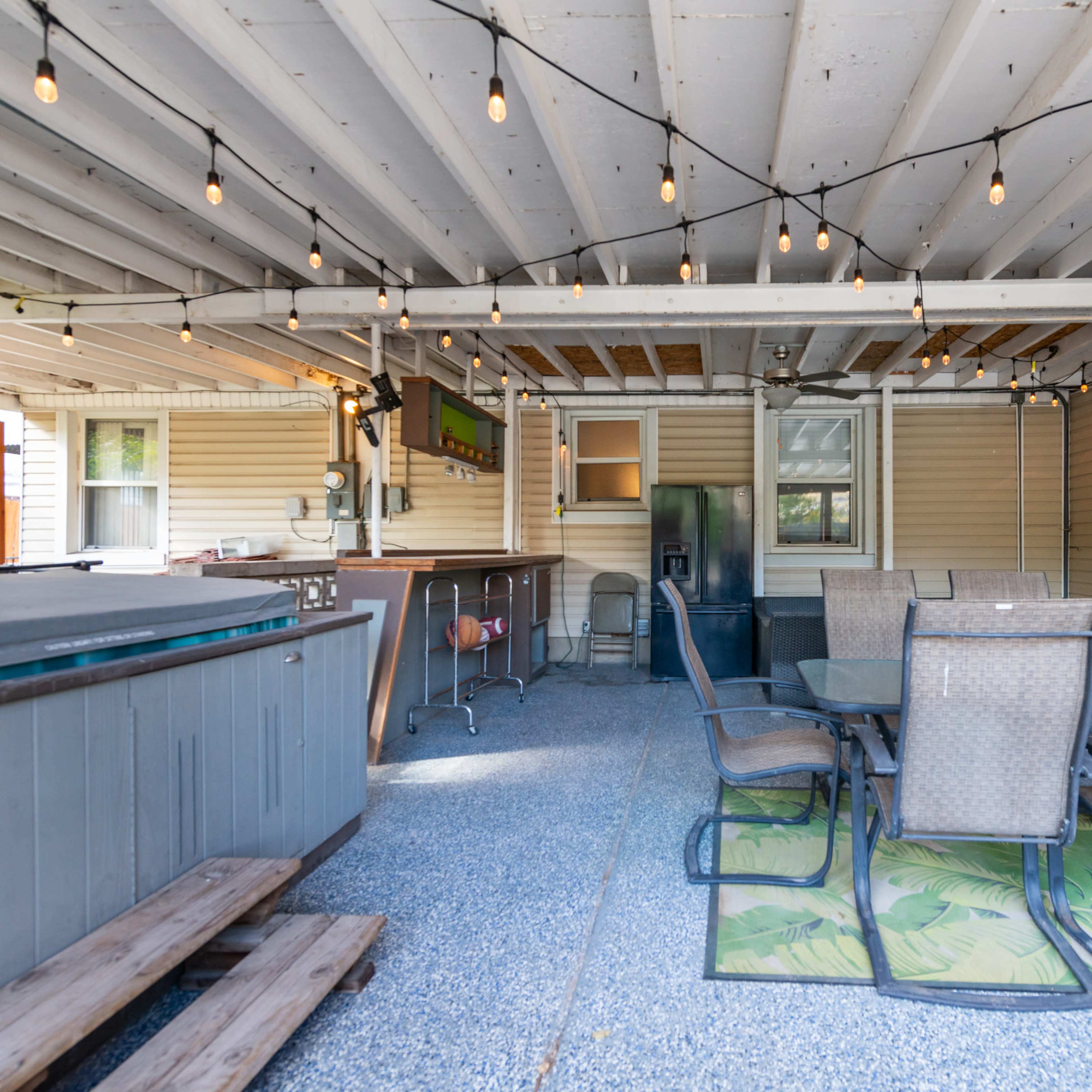 A covered outdoor space with string lights, a dining table, and a hot tub.