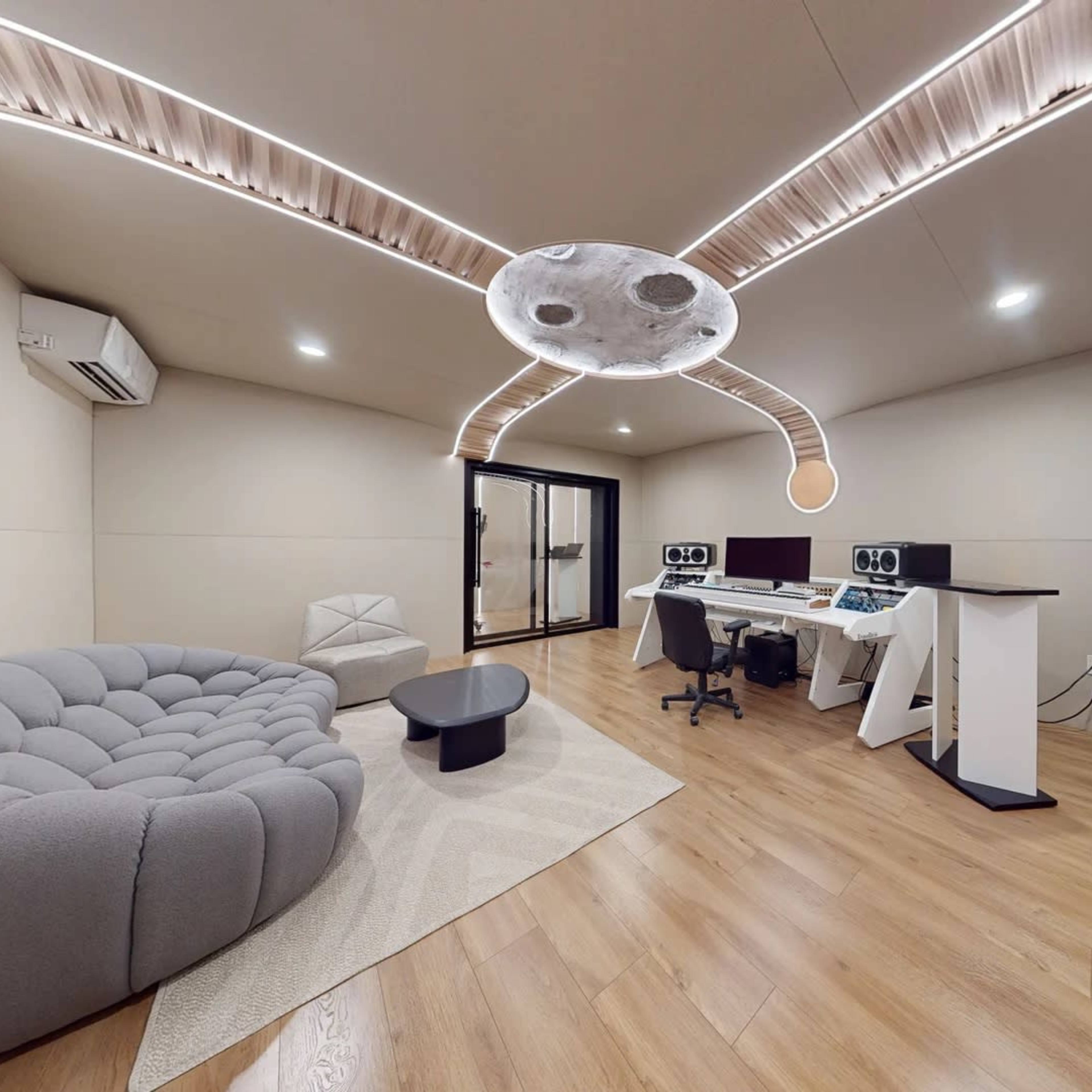 A modern room featuring a curved gray sofa, a small black table, and two computer workstations with a unique ceiling design.