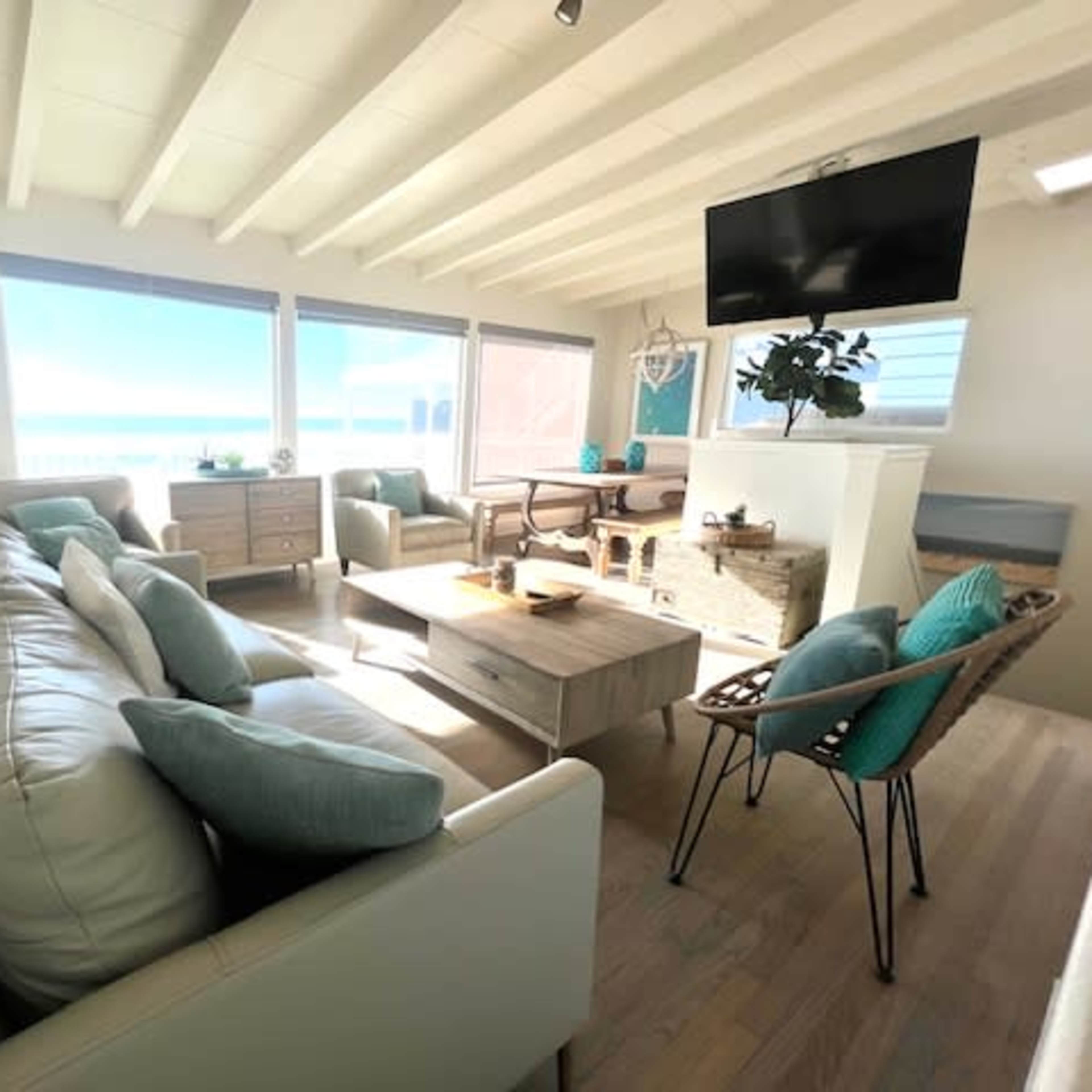 The living room features a light-colored sofa, a wooden coffee table, and large windows that open to a view of the ocean.