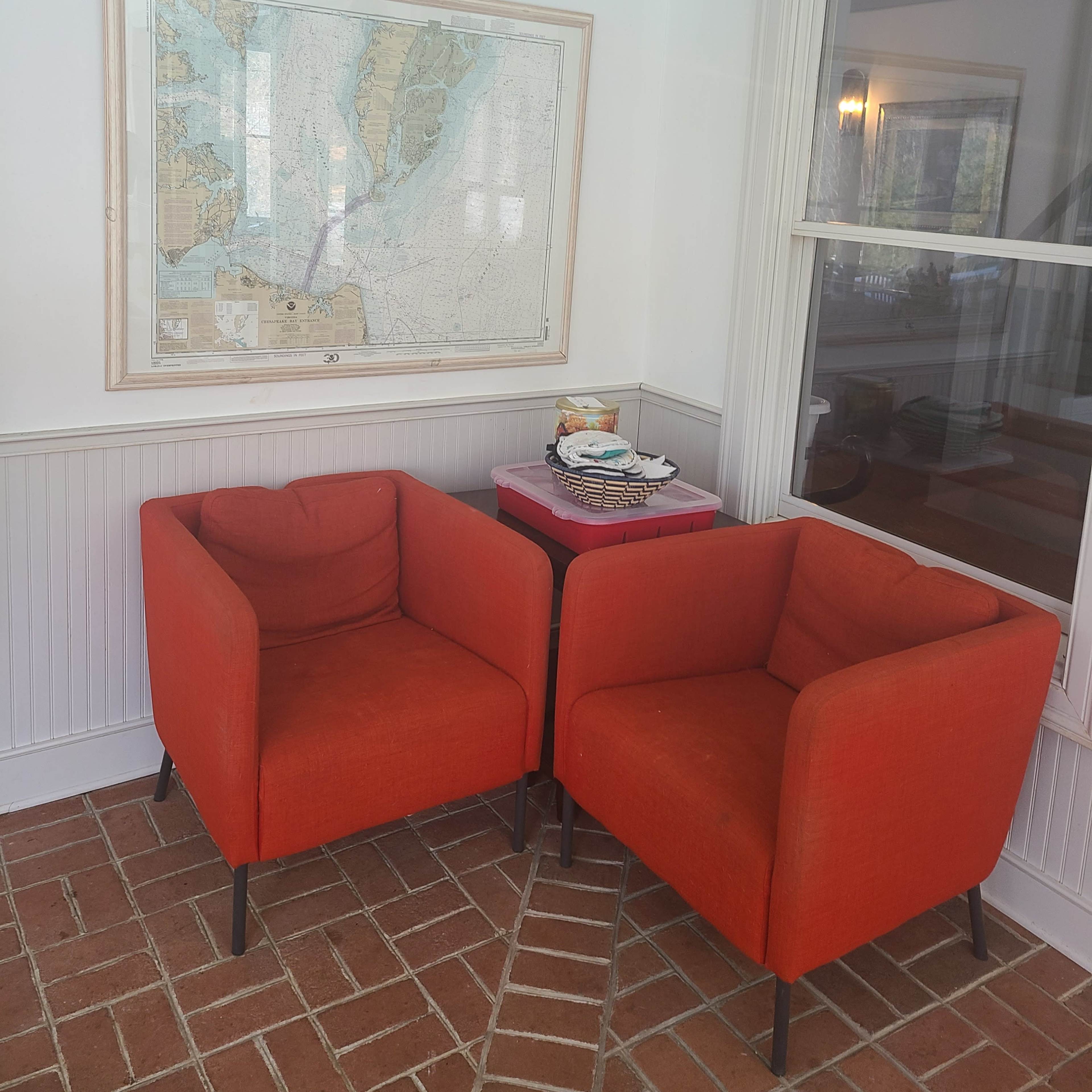 Two orange armchairs are positioned opposite each other near a map hung on the wall and a small table.