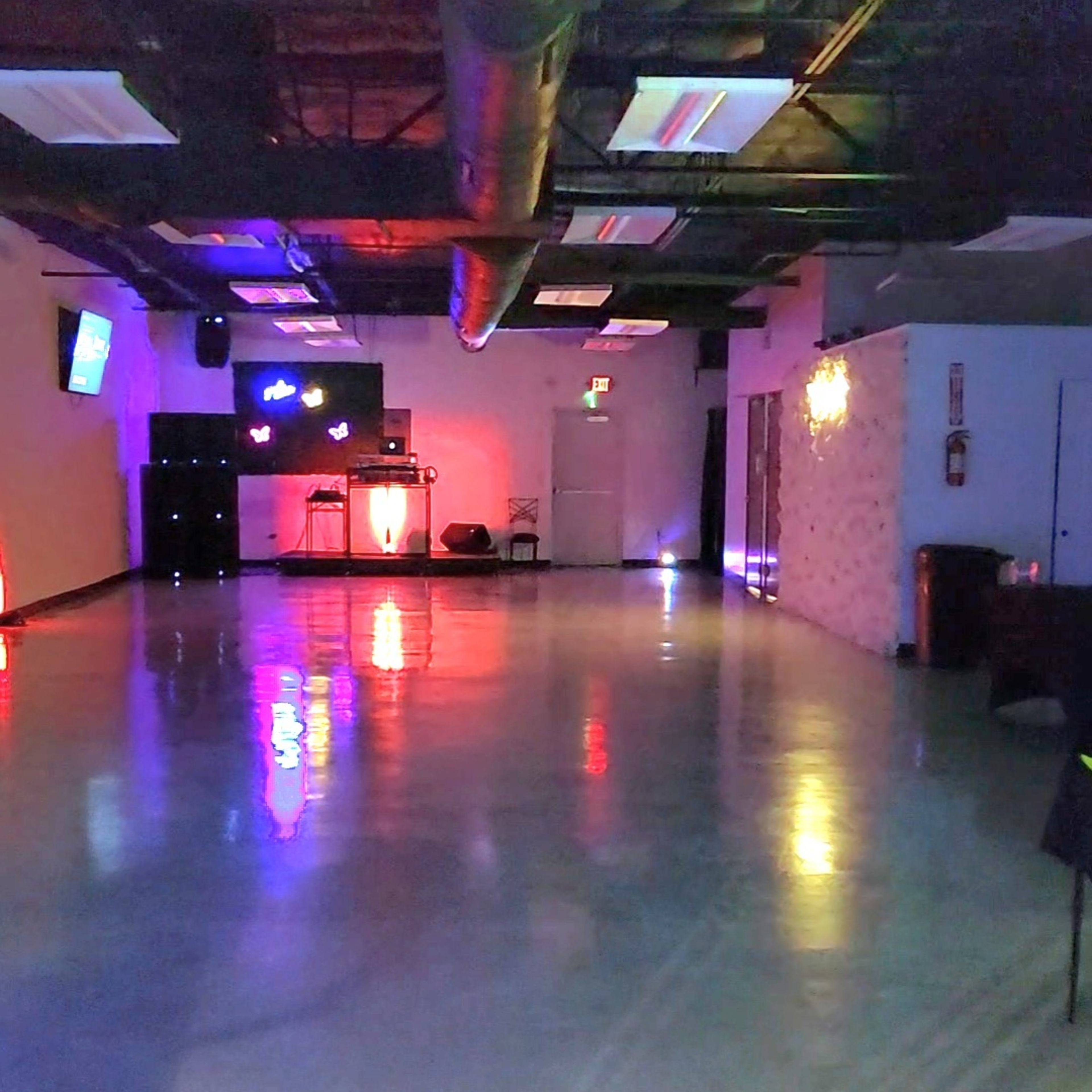 A brightly lit dance studio with colorful lights reflecting off a polished floor and minimal furnishings.