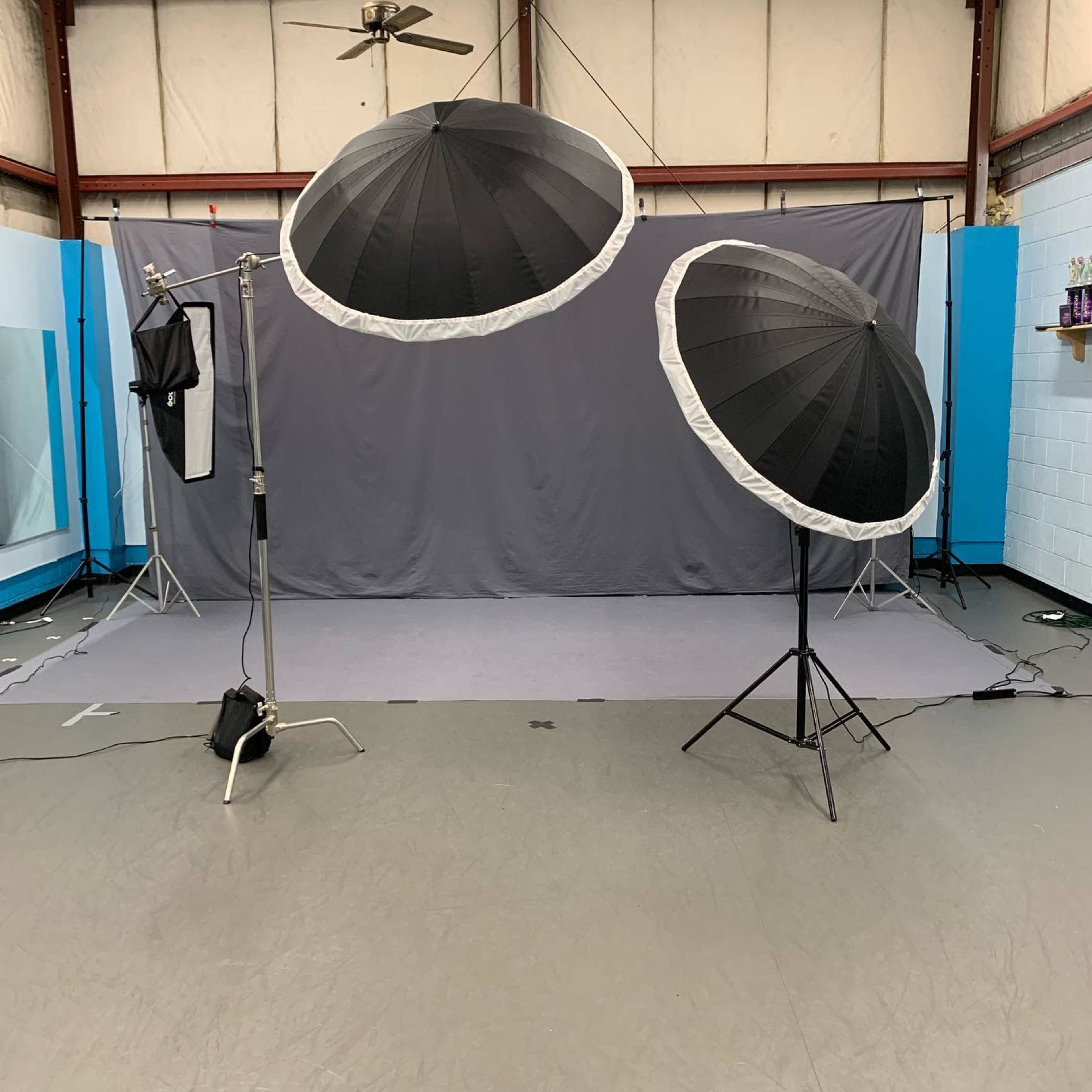 A photography studio setup with two large umbrella softboxes positioned in front of a gray backdrop on a flat floor.