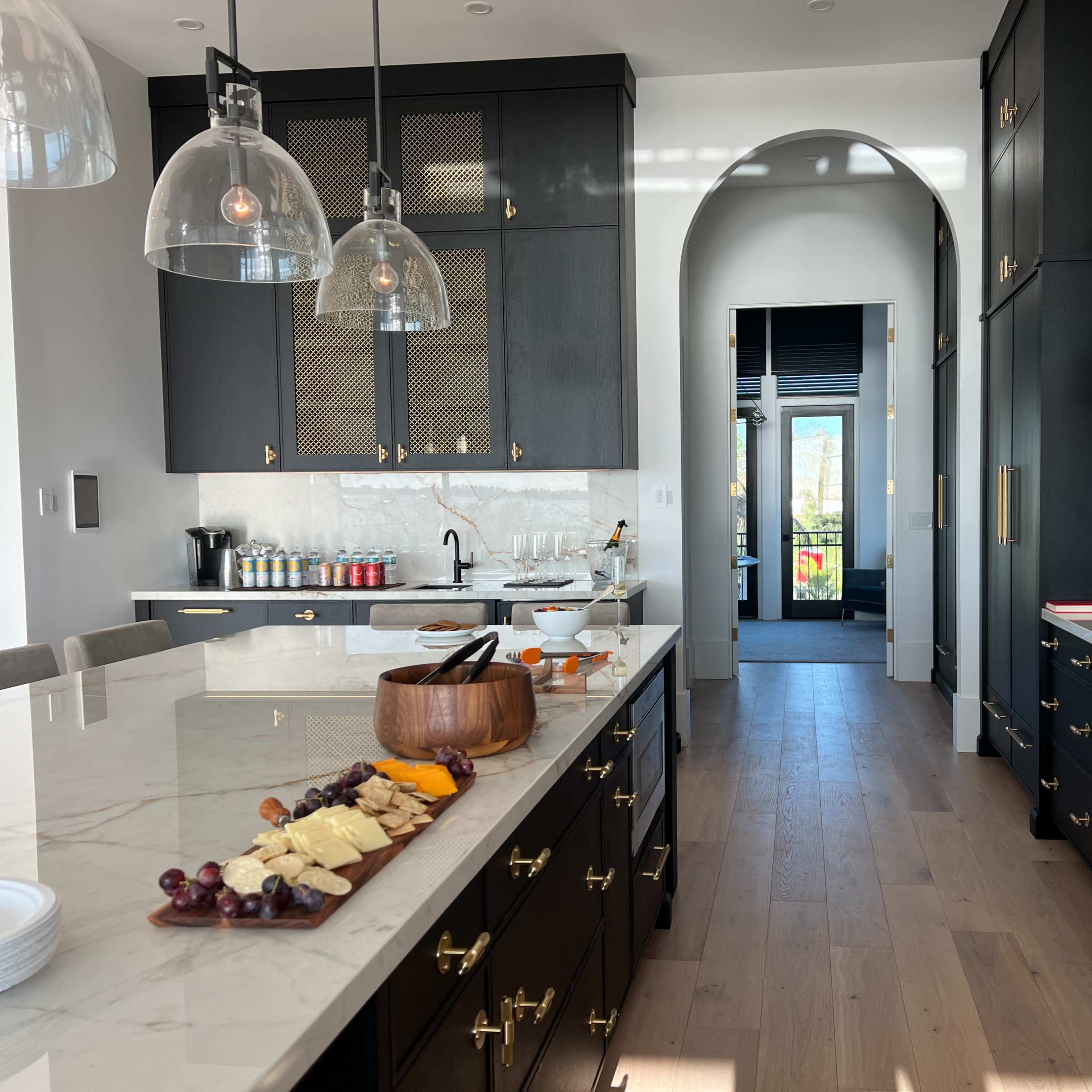 A modern kitchen features dark cabinetry, a marble countertop with a charcuterie board, and large pendant lights above the island.