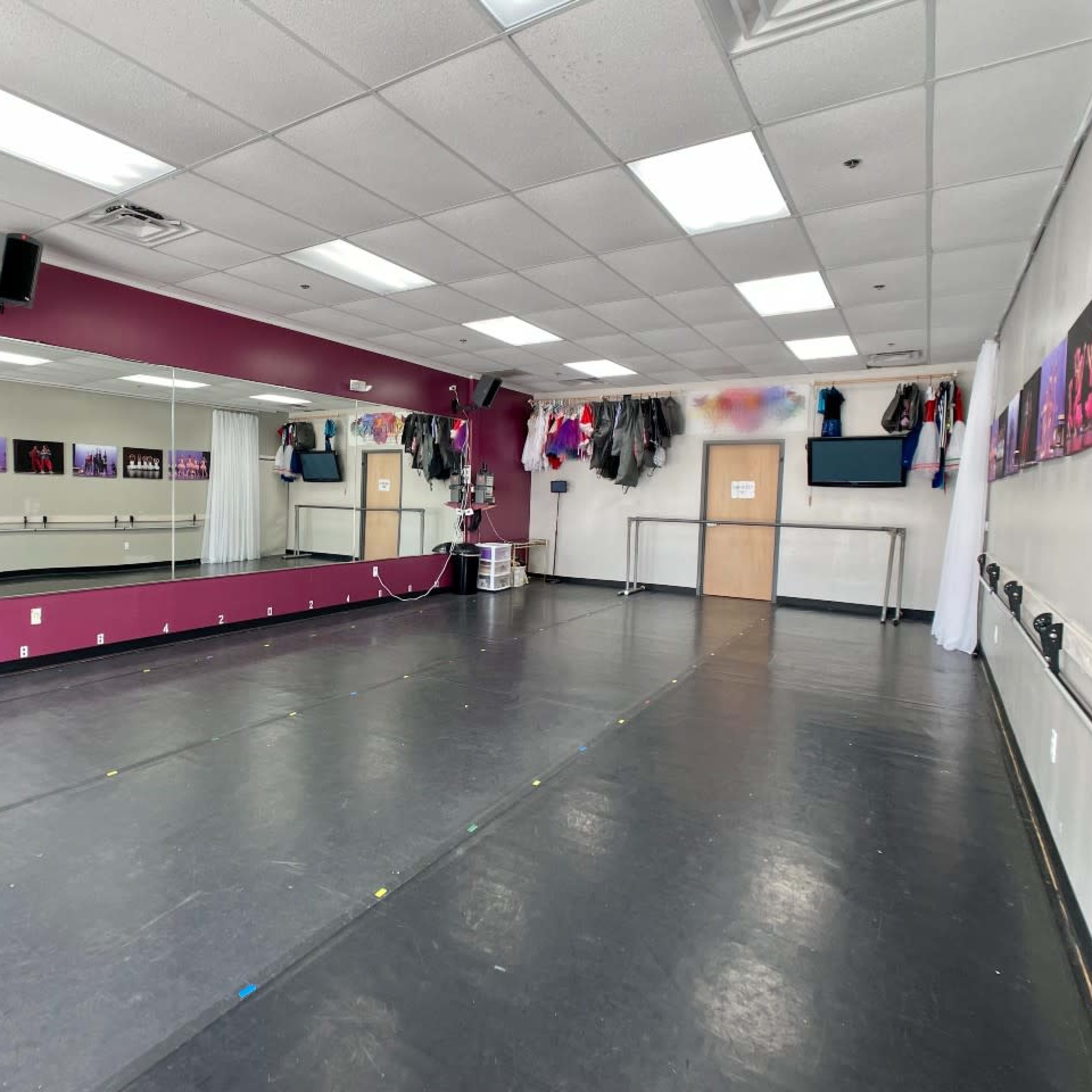 A spacious dance studio with a mirrored wall, a dark floor, and various costumes hanging on the walls.