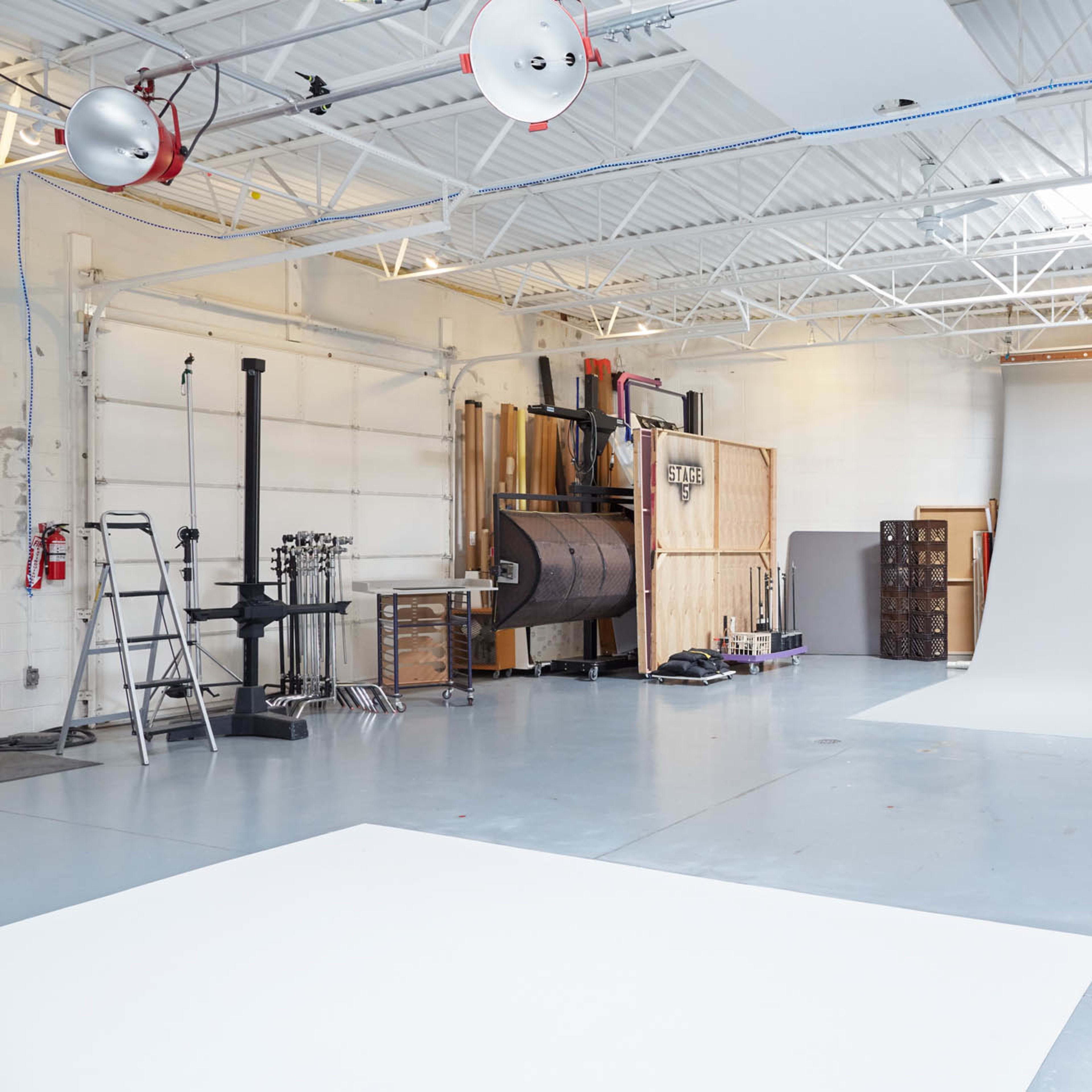 A spacious photography studio with a white backdrop, lighting equipment, and various tools along the walls.