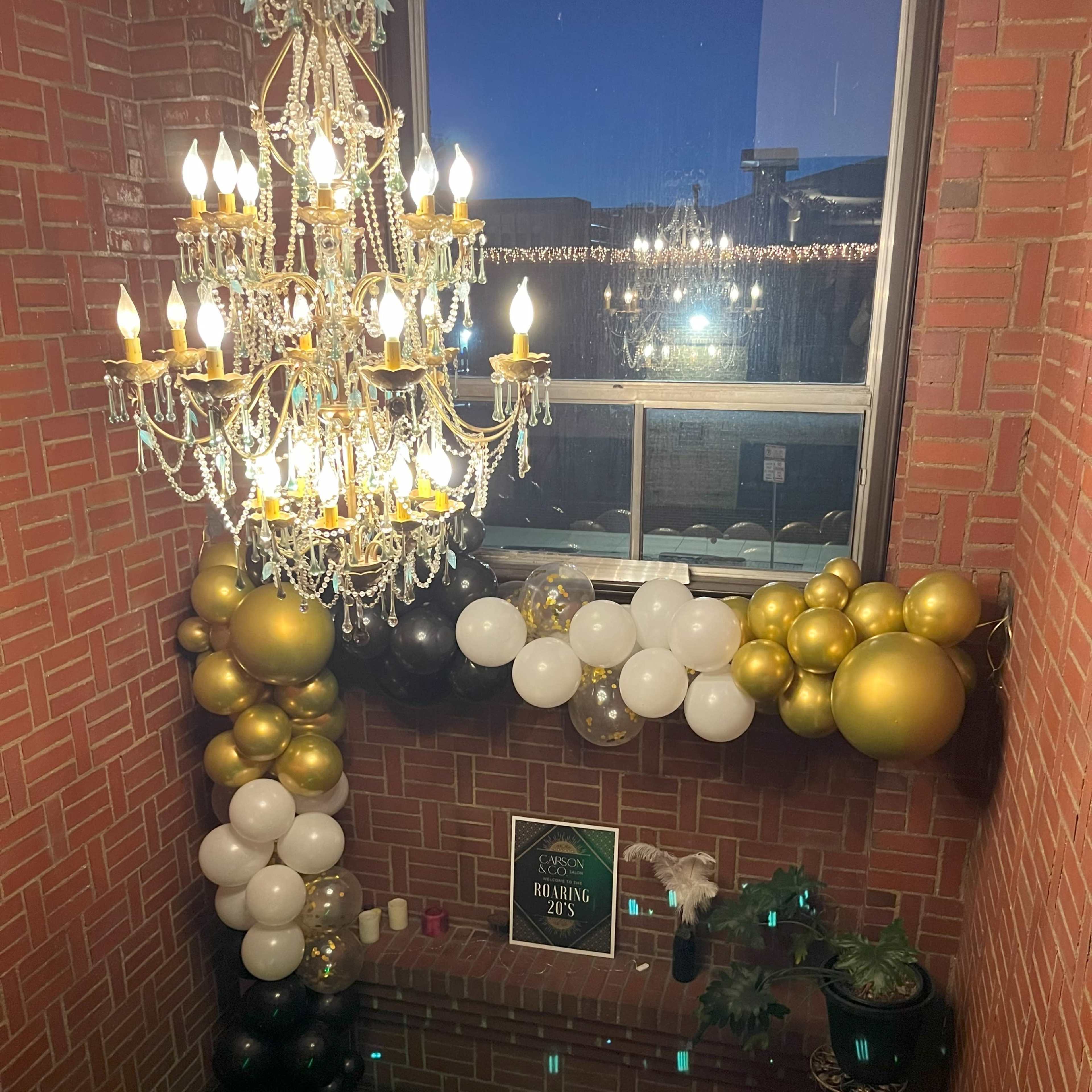 A staircase decorated with a chandelier and an arrangement of black, white, and gold balloons along the walls.
