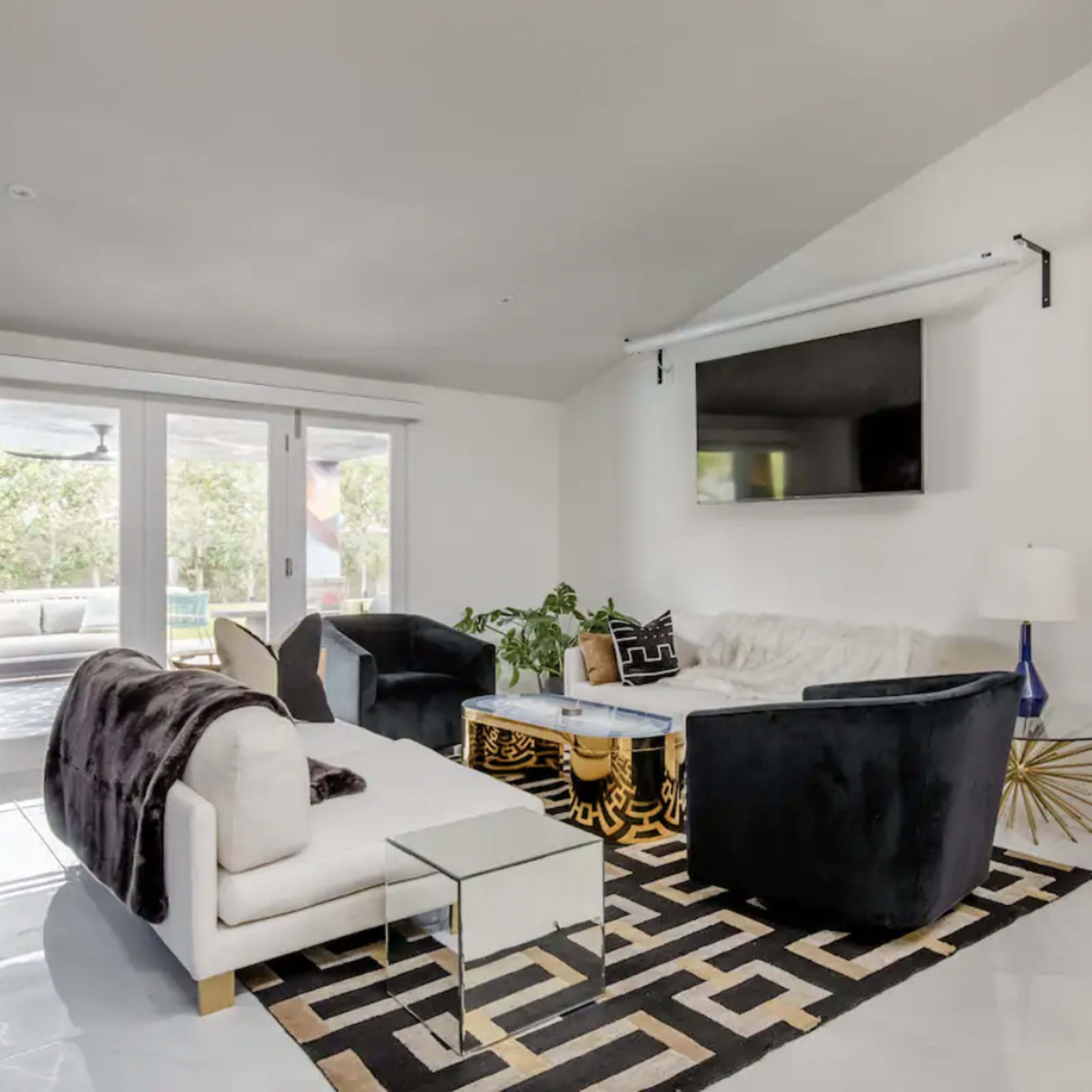 A modern living room with a white sofa, black armchairs, a geometric rug, and a fireplace.