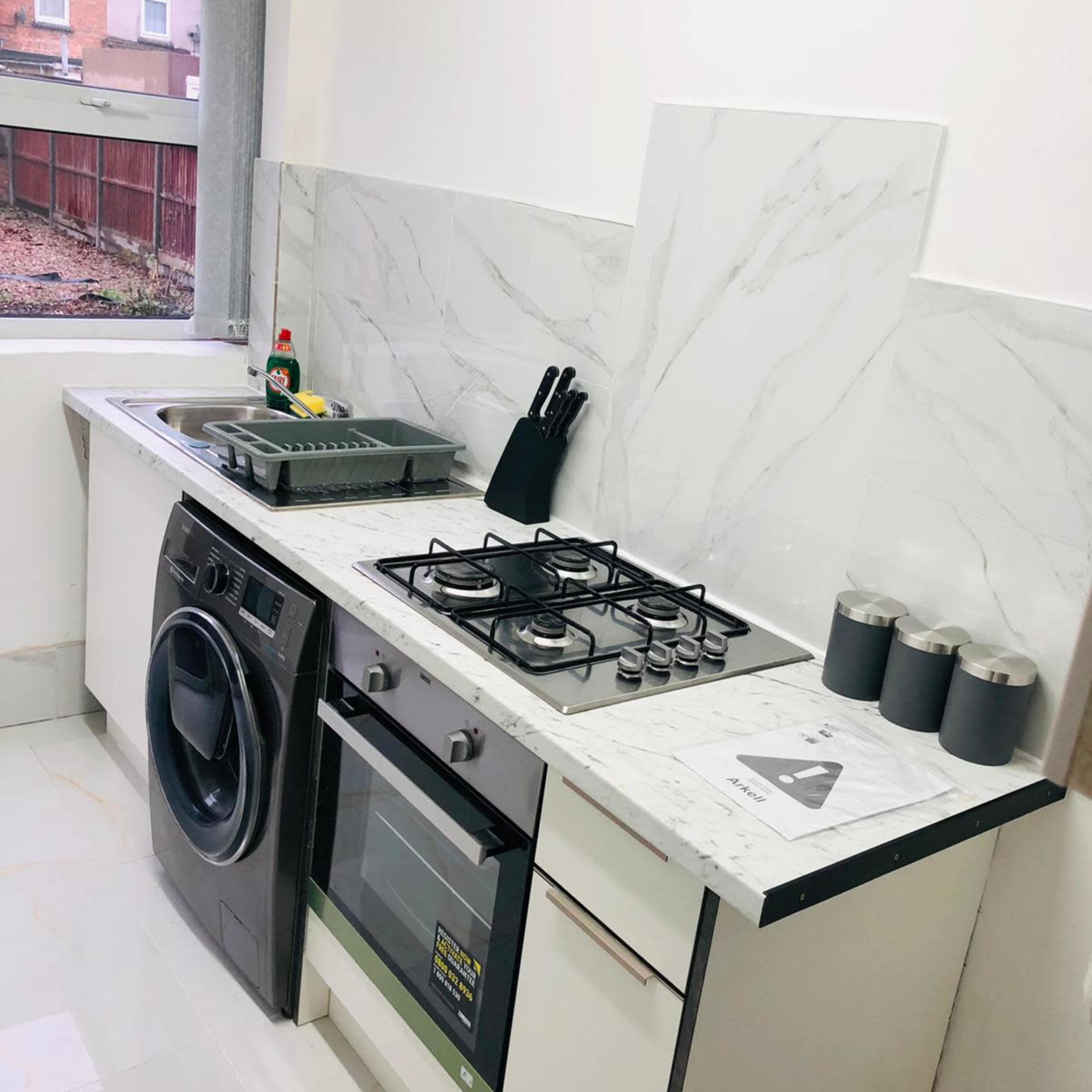 A modern kitchen with a gas stove, an oven, a washing machine, and a marble countertop.