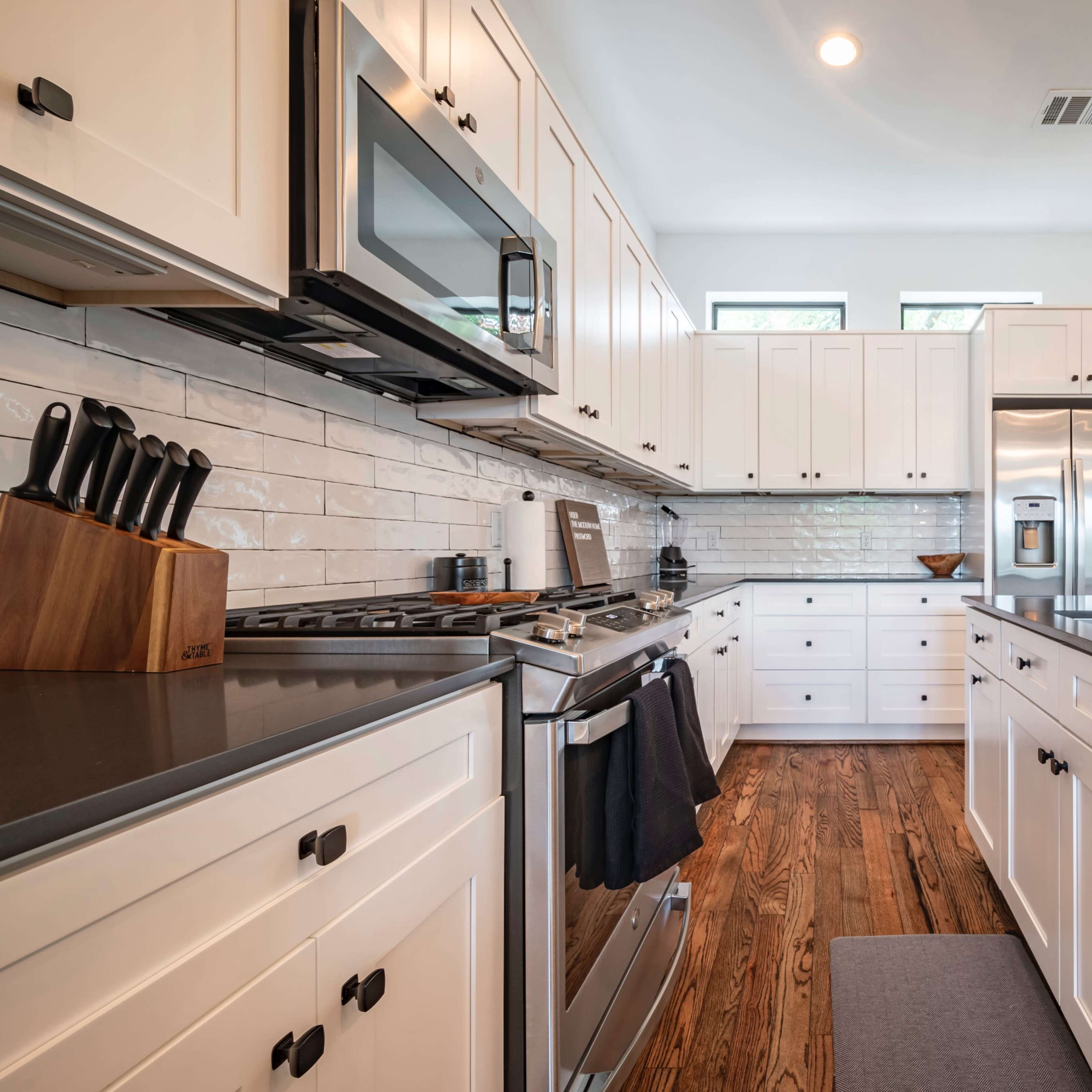A modern kitchen features white cabinetry, stainless steel appliances, and hardwood flooring.