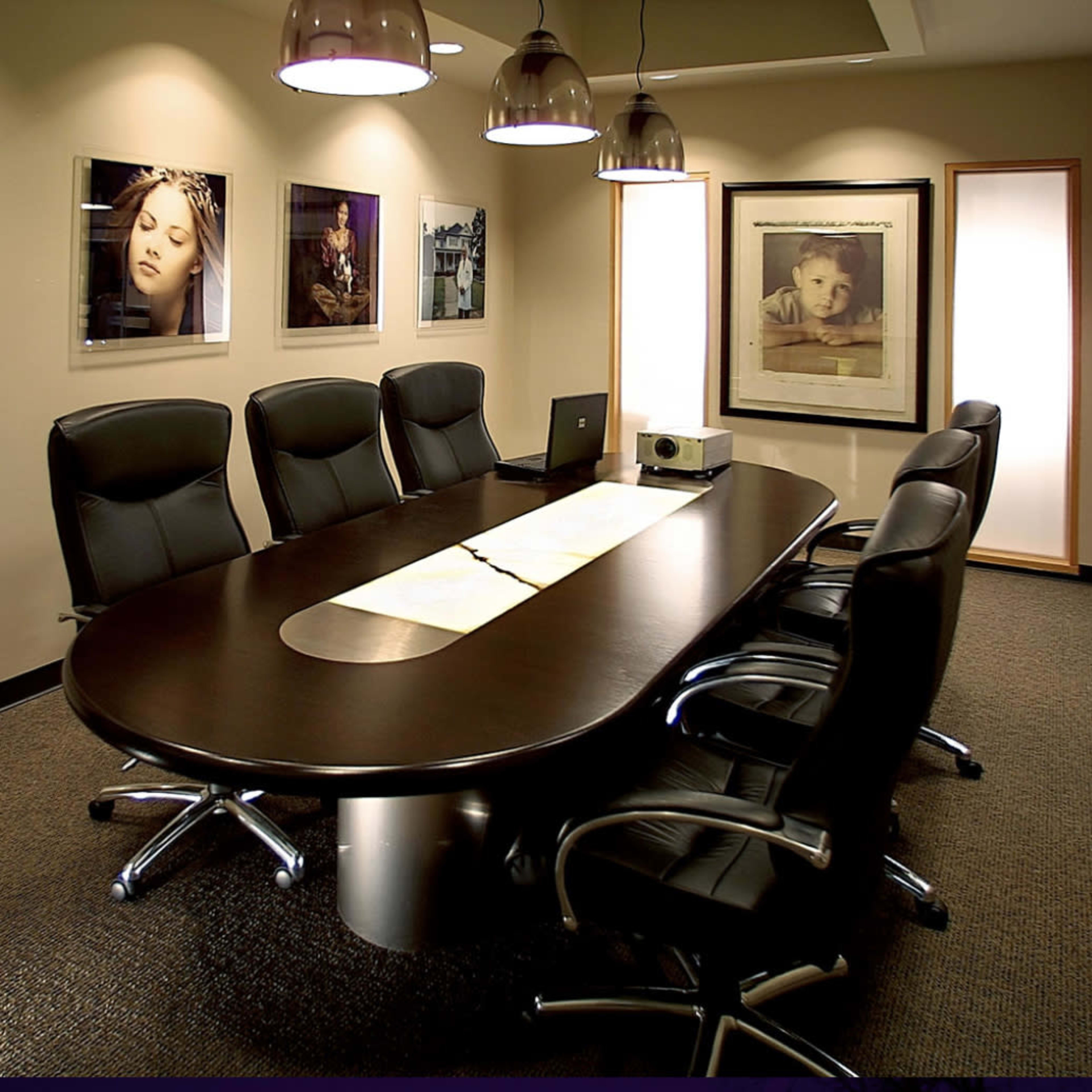 A conference room features an oval table surrounded by black leather chairs, with framed photographs displayed on the walls.