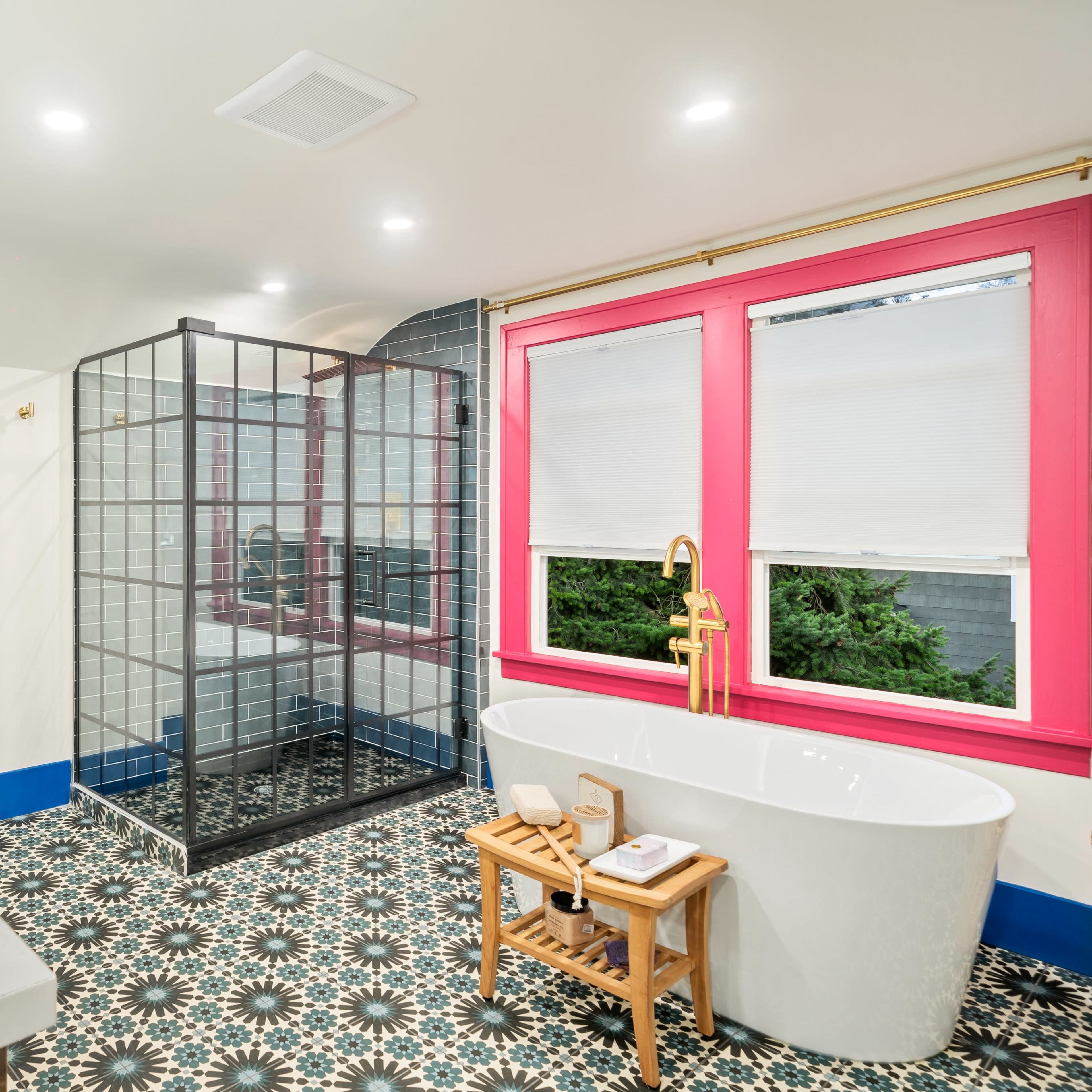 The bathroom features a glass shower, a freestanding bathtub, and patterned floor tiles, with bright trim around the windows.