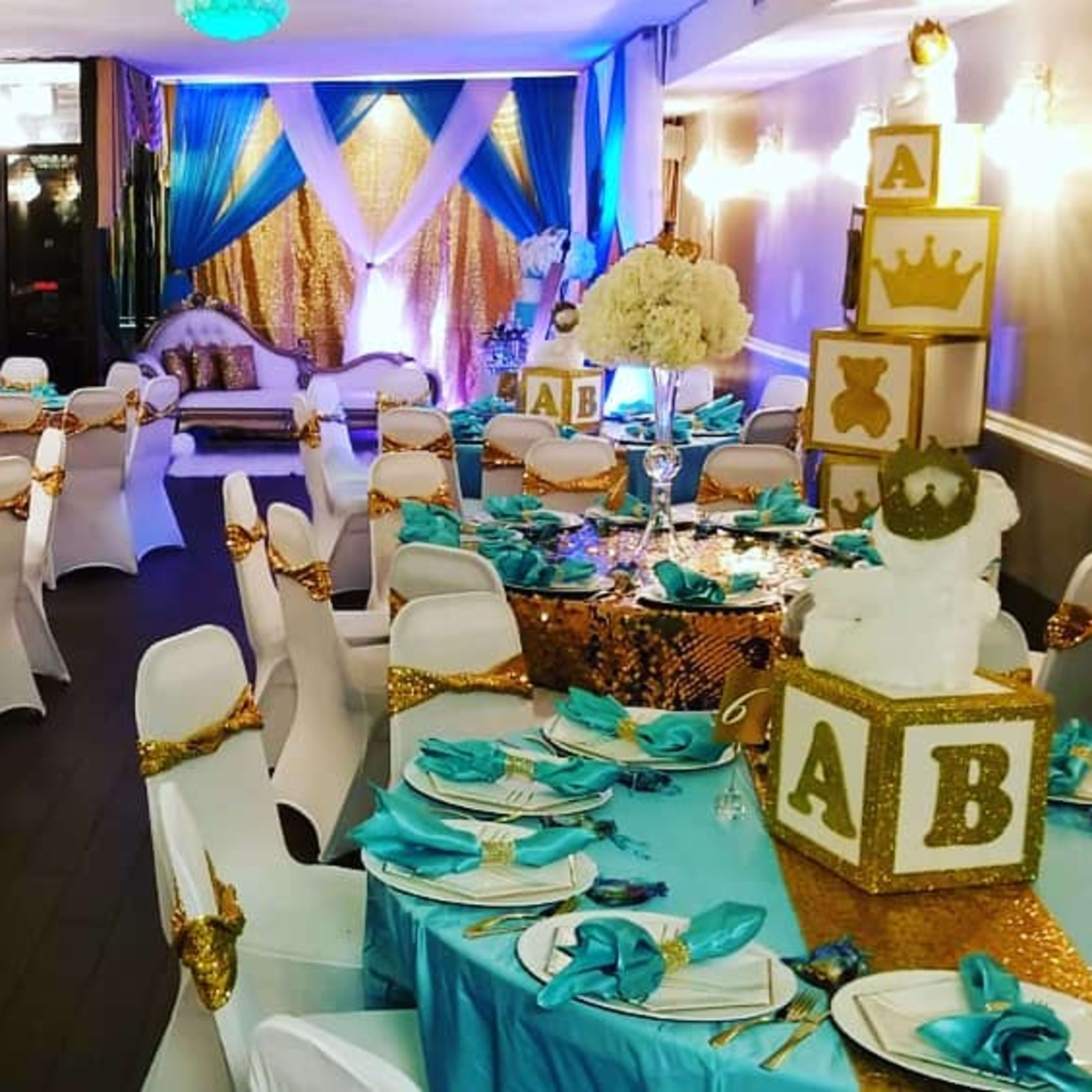 A banquet hall elegantly decorated with turquoise and gold tablecloths, ornate centerpieces, and large decorative letter blocks arranged on a table.