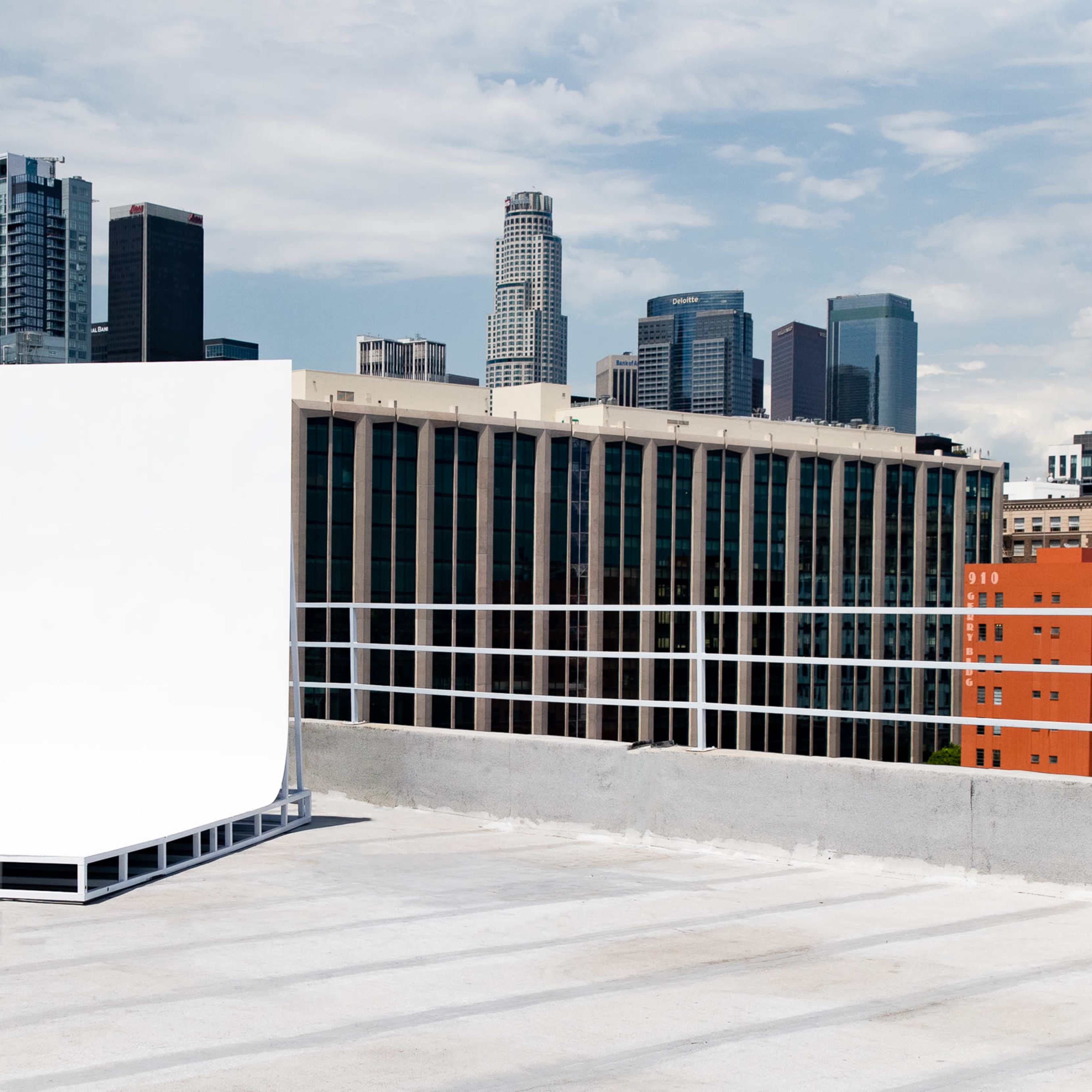 A large white backdrop is positioned on a rooftop overlooking a city skyline with several tall buildings.