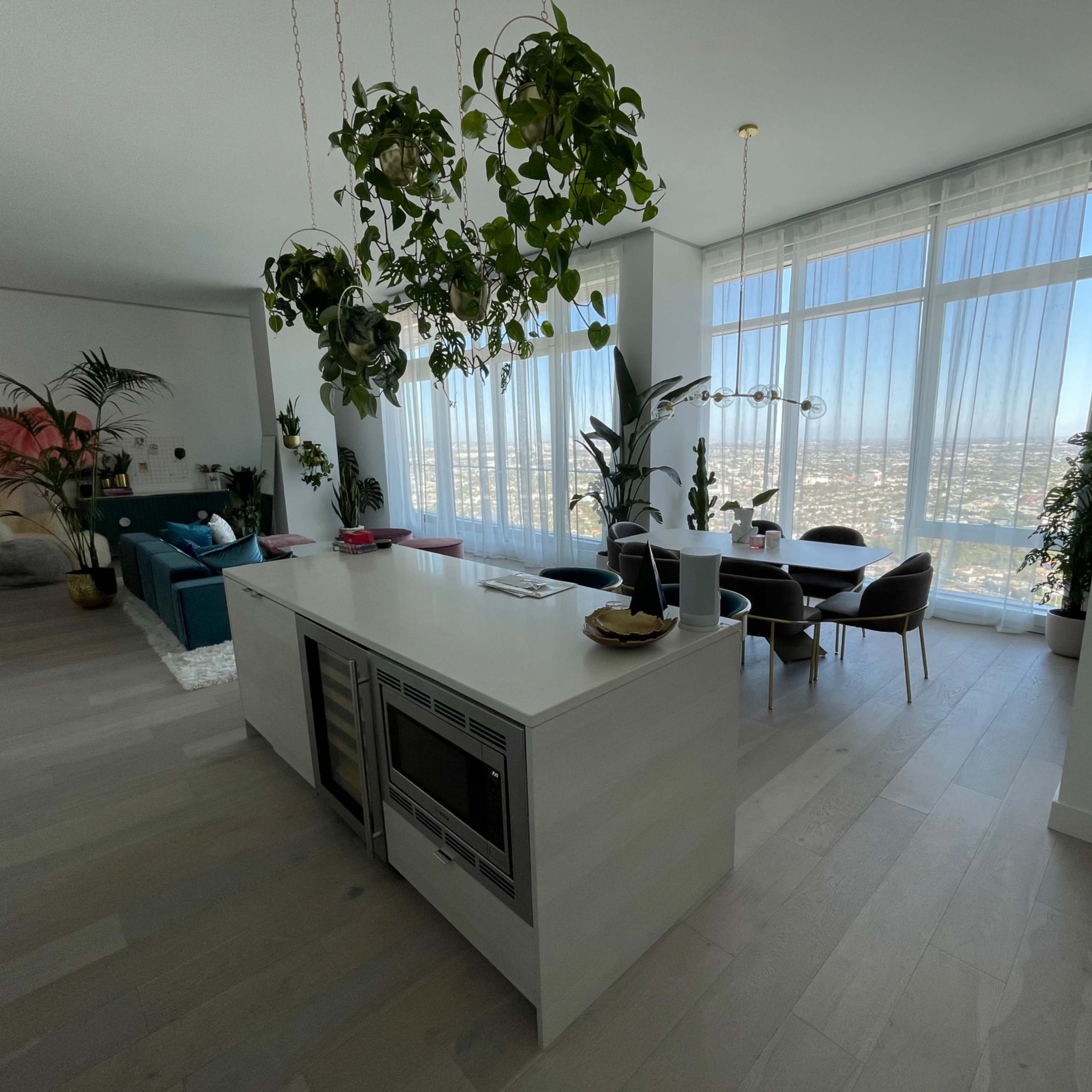 A modern open-concept living space features a kitchen island, dining area, and large windows with views of the city.