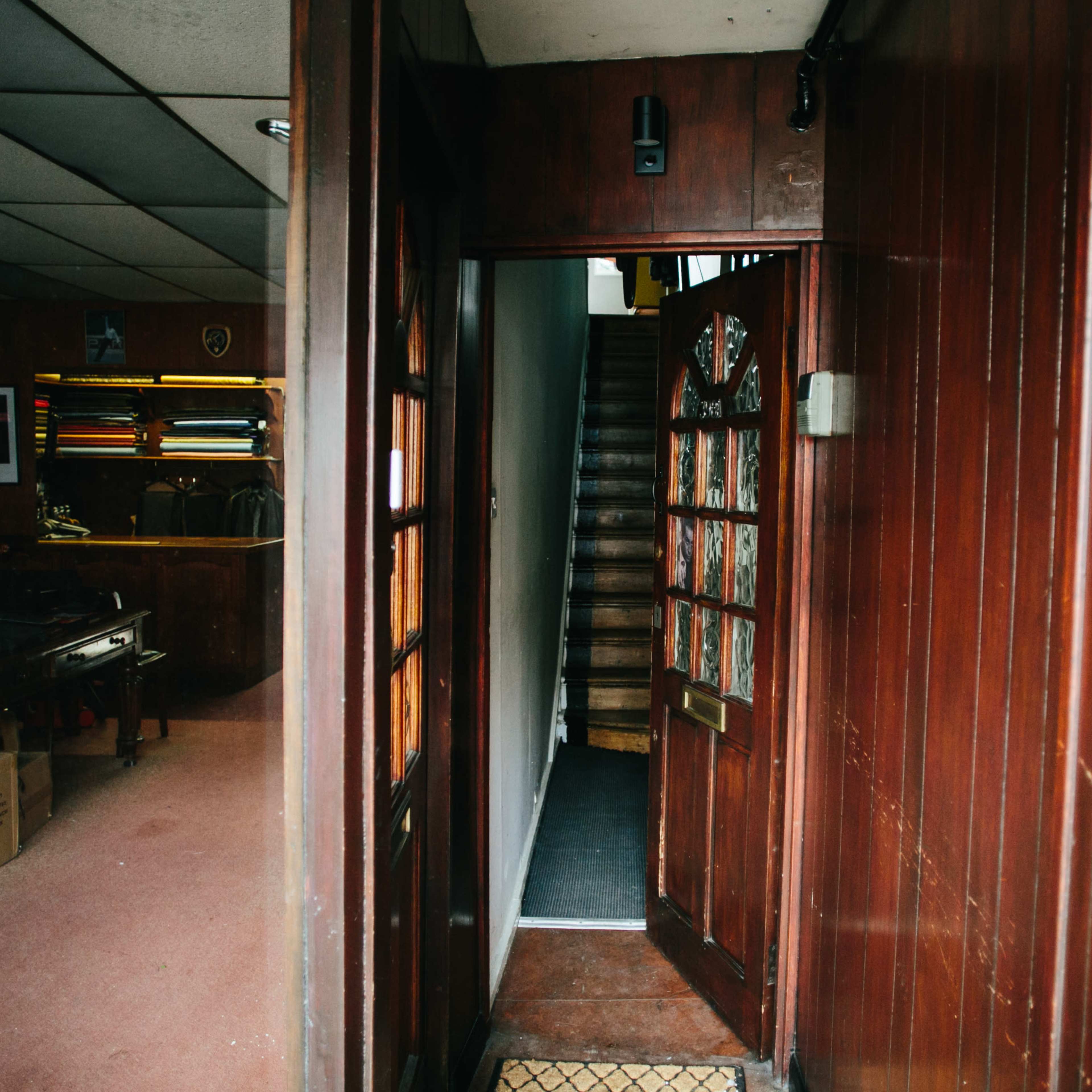 A wooden door leads into a dimly lit hallway with stairs ascending to the upper level.