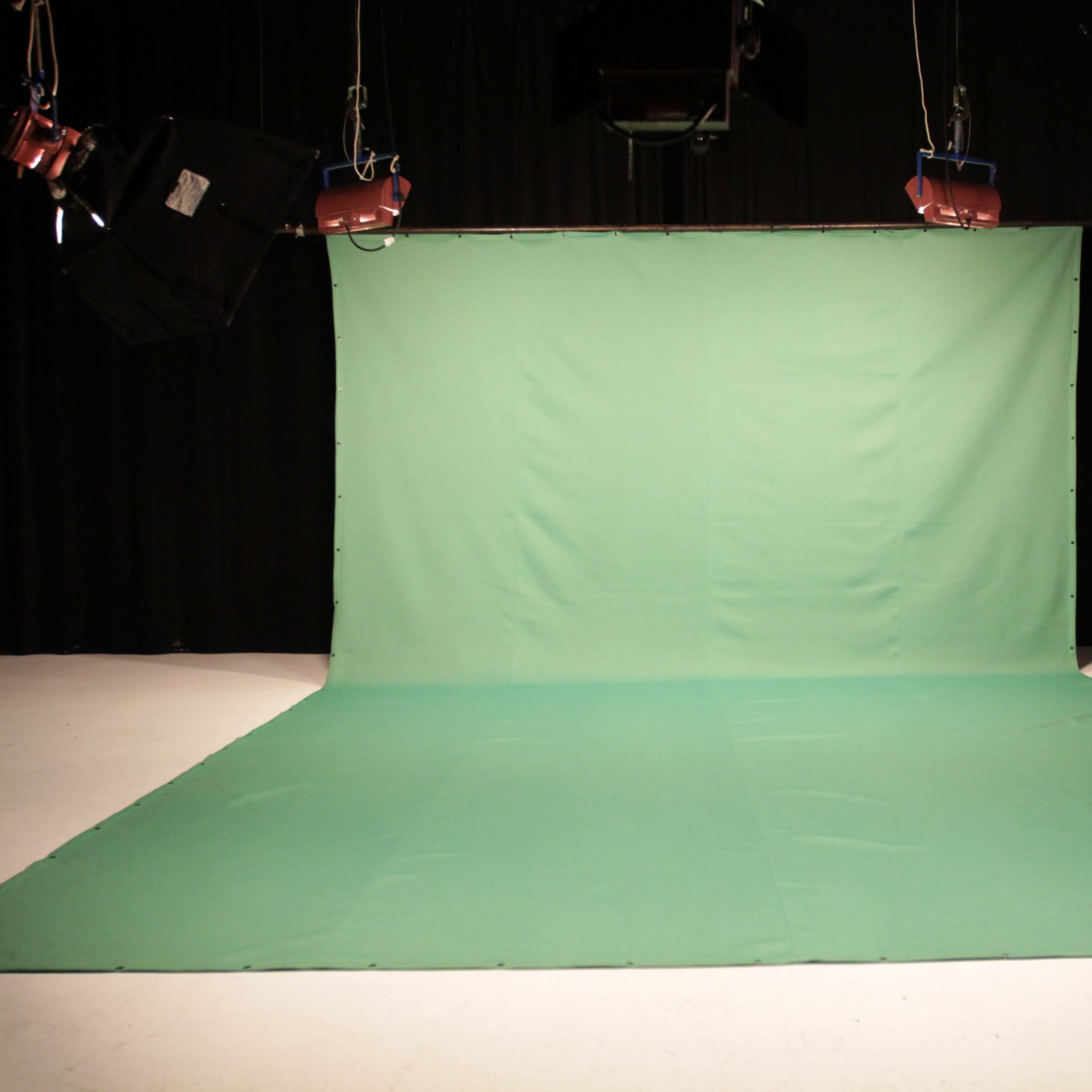 A green backdrop set up in a studio with lighting rigs overhead.