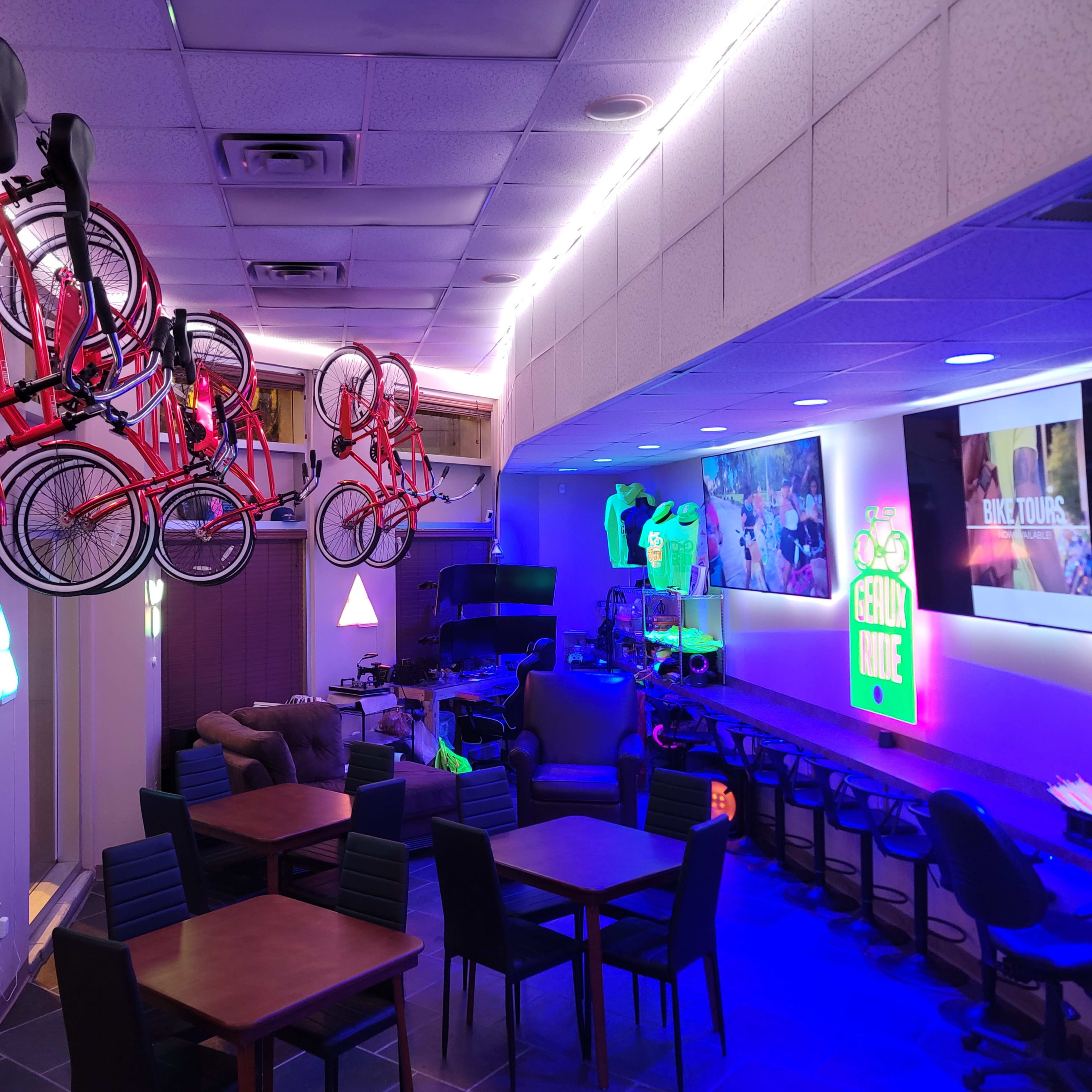 The interior of a vibrant café features hanging red bicycles, colorful neon lights, and a cozy seating area with dark wooden tables.