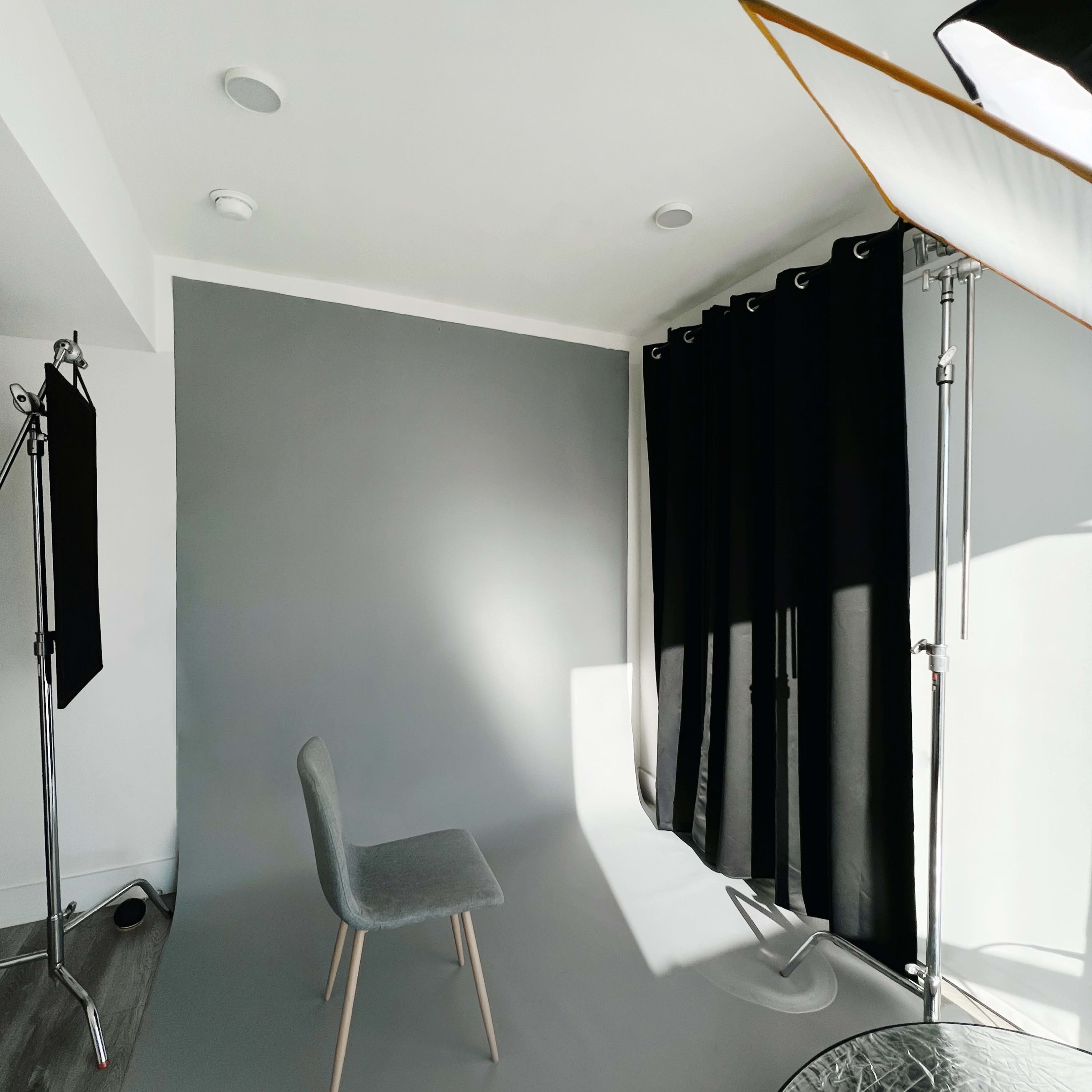 A minimalist photography studio with a chair positioned on a gray backdrop, illuminated by soft lighting.