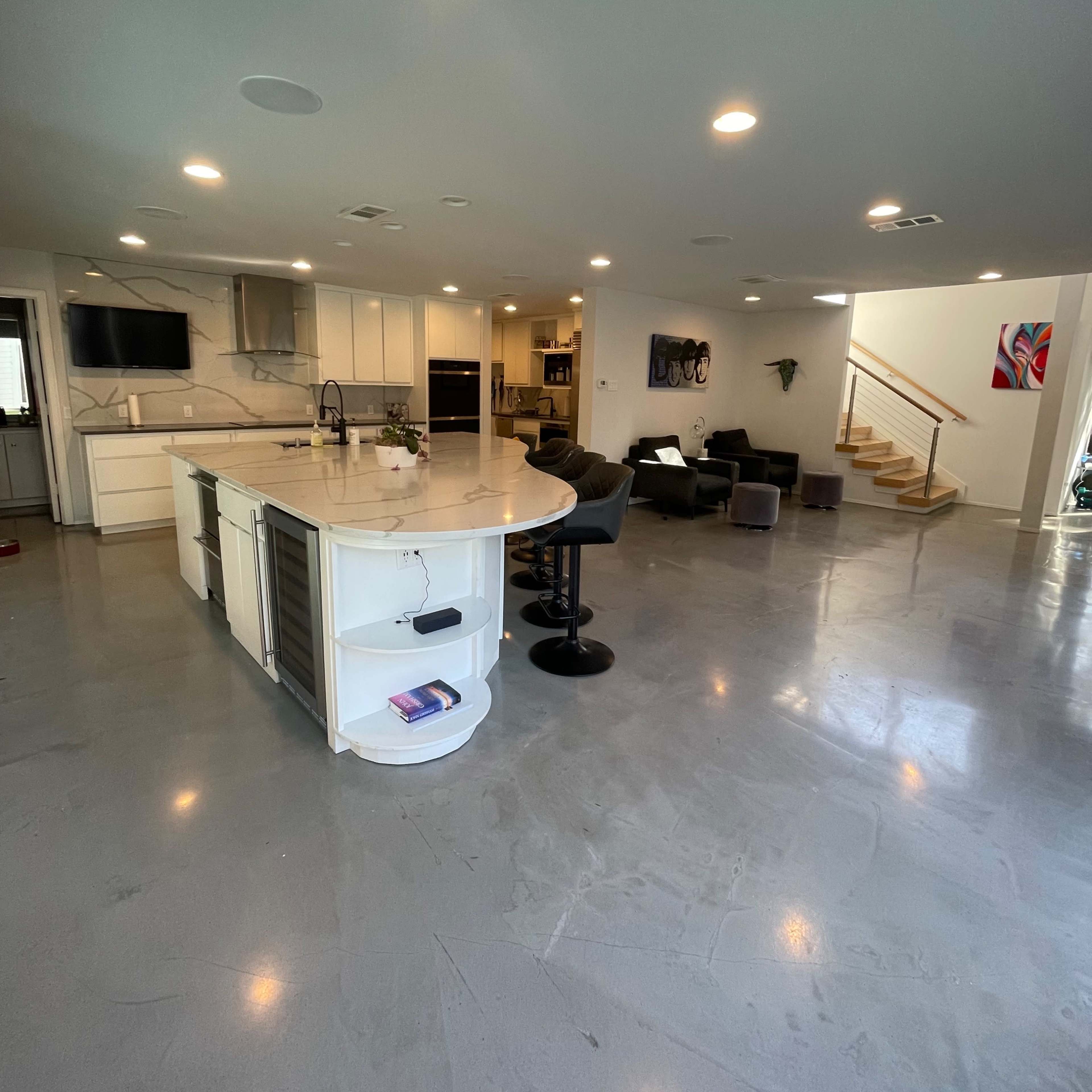 A modern kitchen with a large island, sleek countertops, and an open living area featuring a staircase and seating.