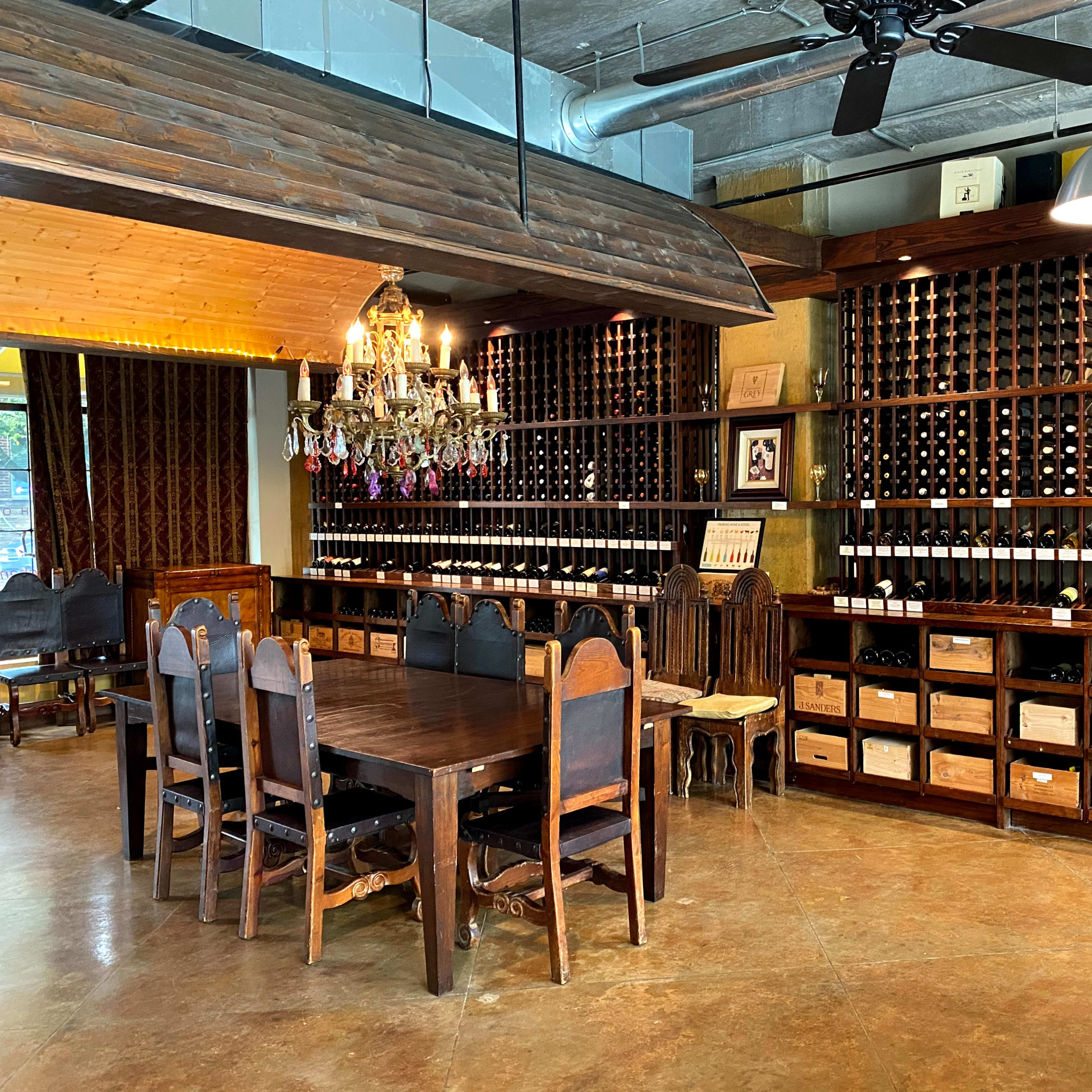 A wine-tasting room with wooden shelves filled with bottles of wine, a large wooden dining table, and a chandelier hanging from the ceiling.