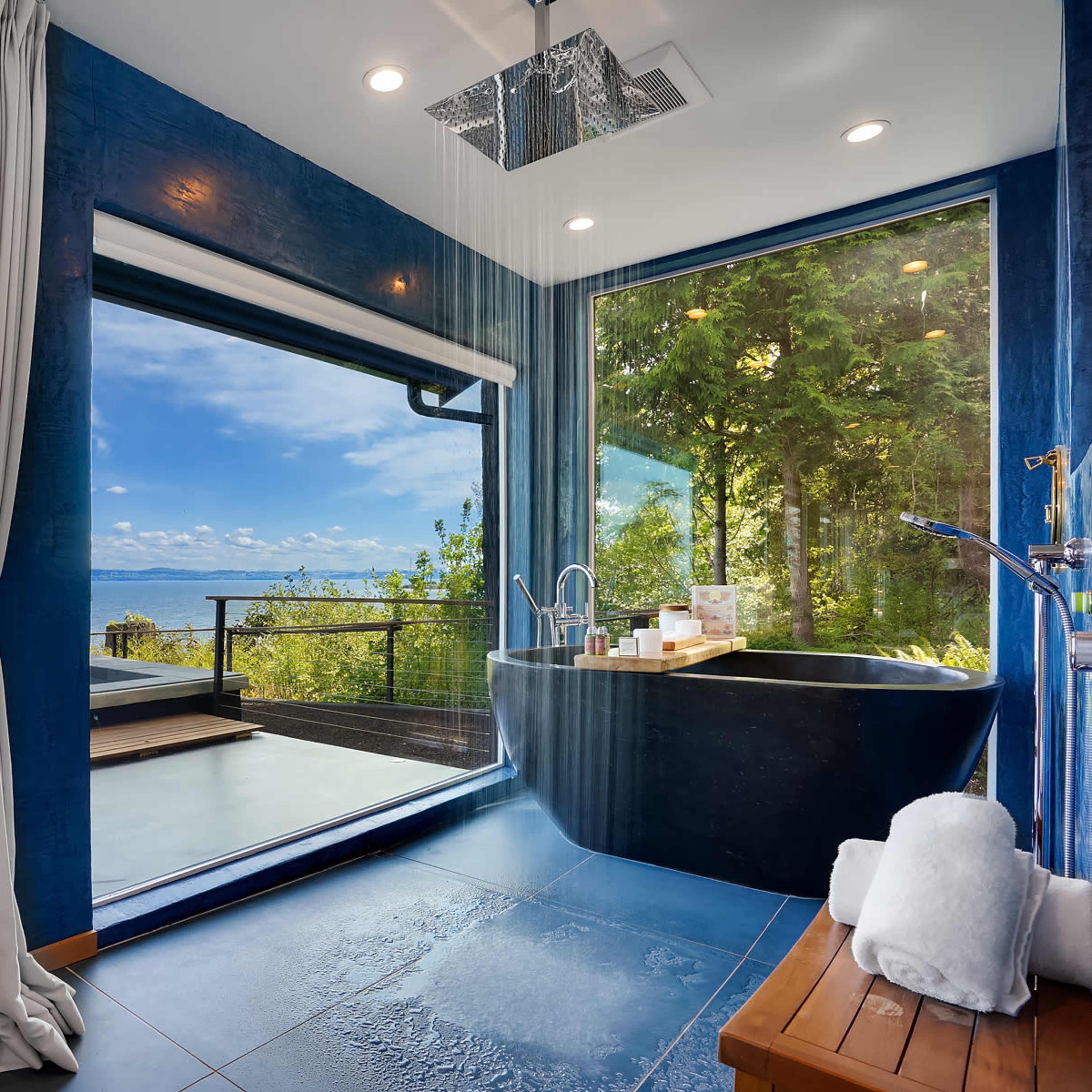 A modern bathroom featuring a large bathtub and floor-to-ceiling windows that provide a view of a water landscape and greenery.