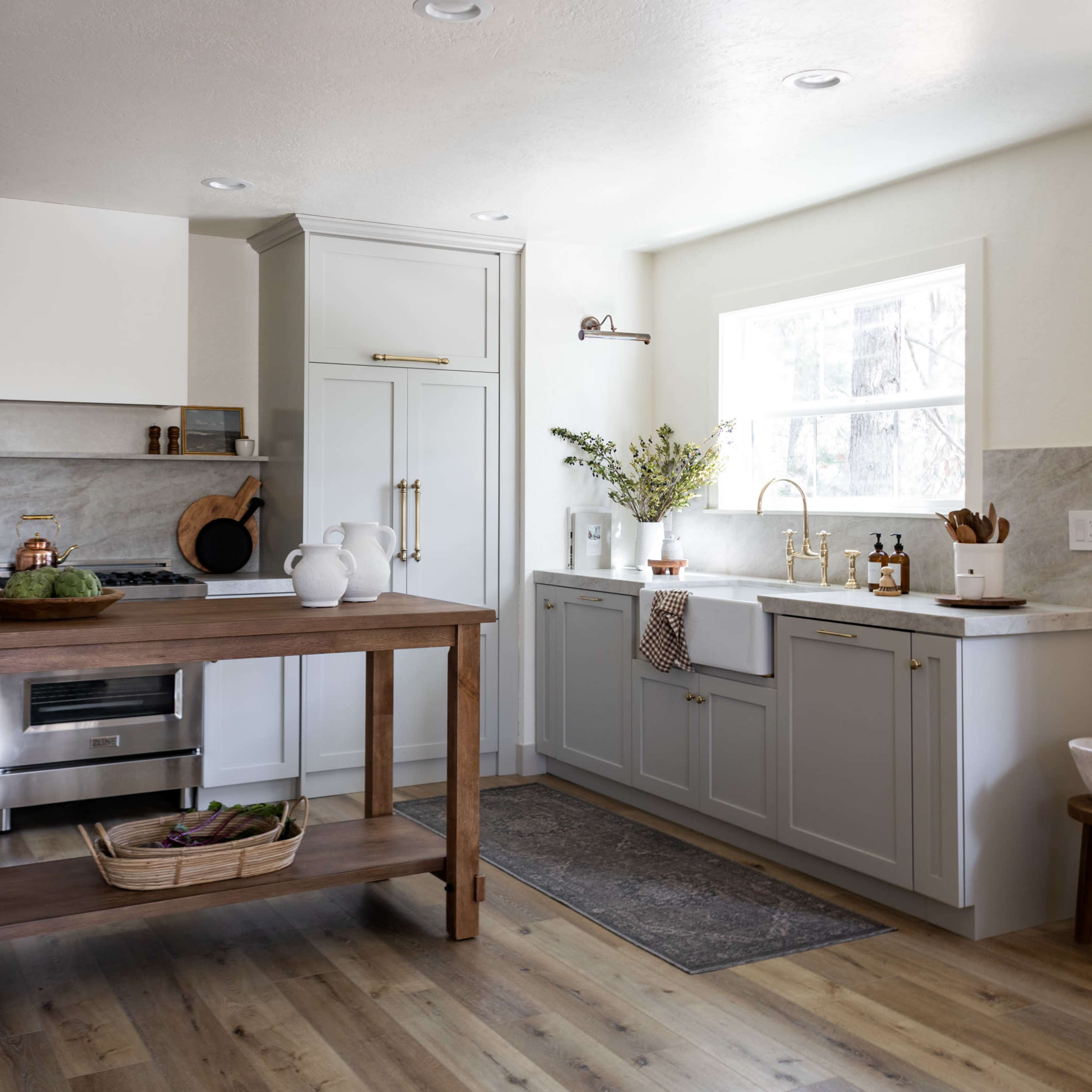 A modern kitchen with gray cabinetry, a wooden island, a window above the sink, and a light-colored floor.