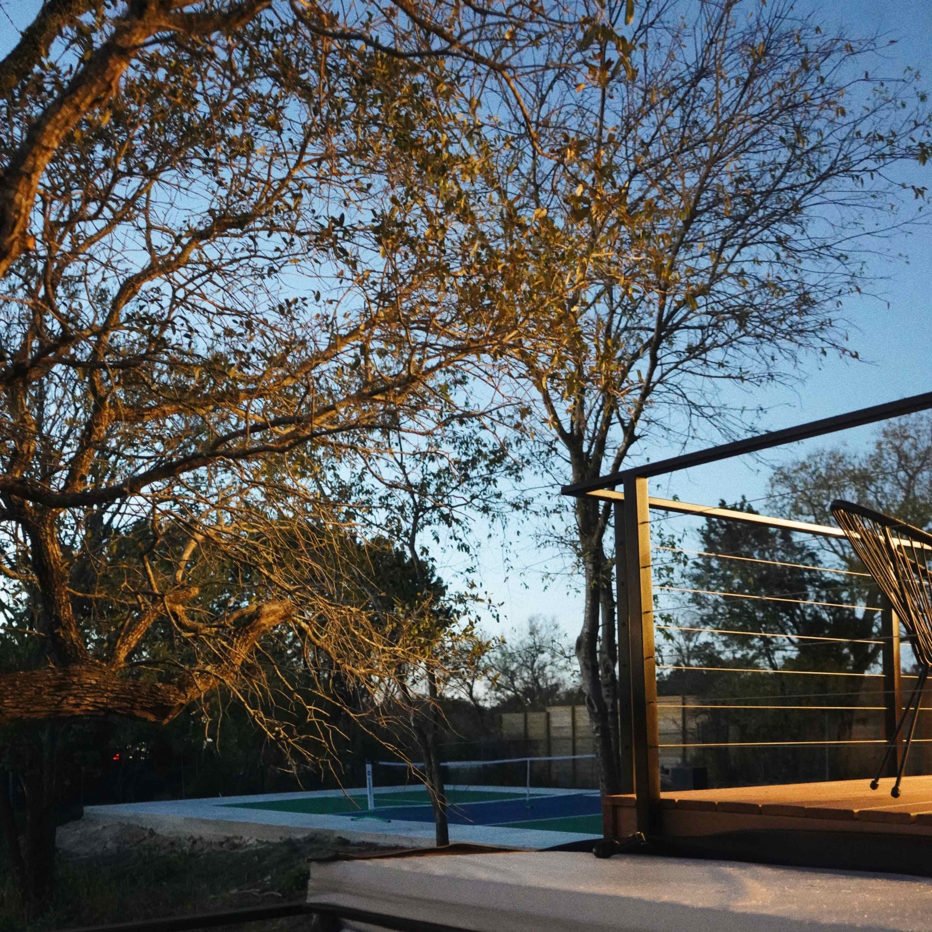 A pink floating ball rests in a hot tub beside a tree as twilight sets in, with a pool visible in the background.