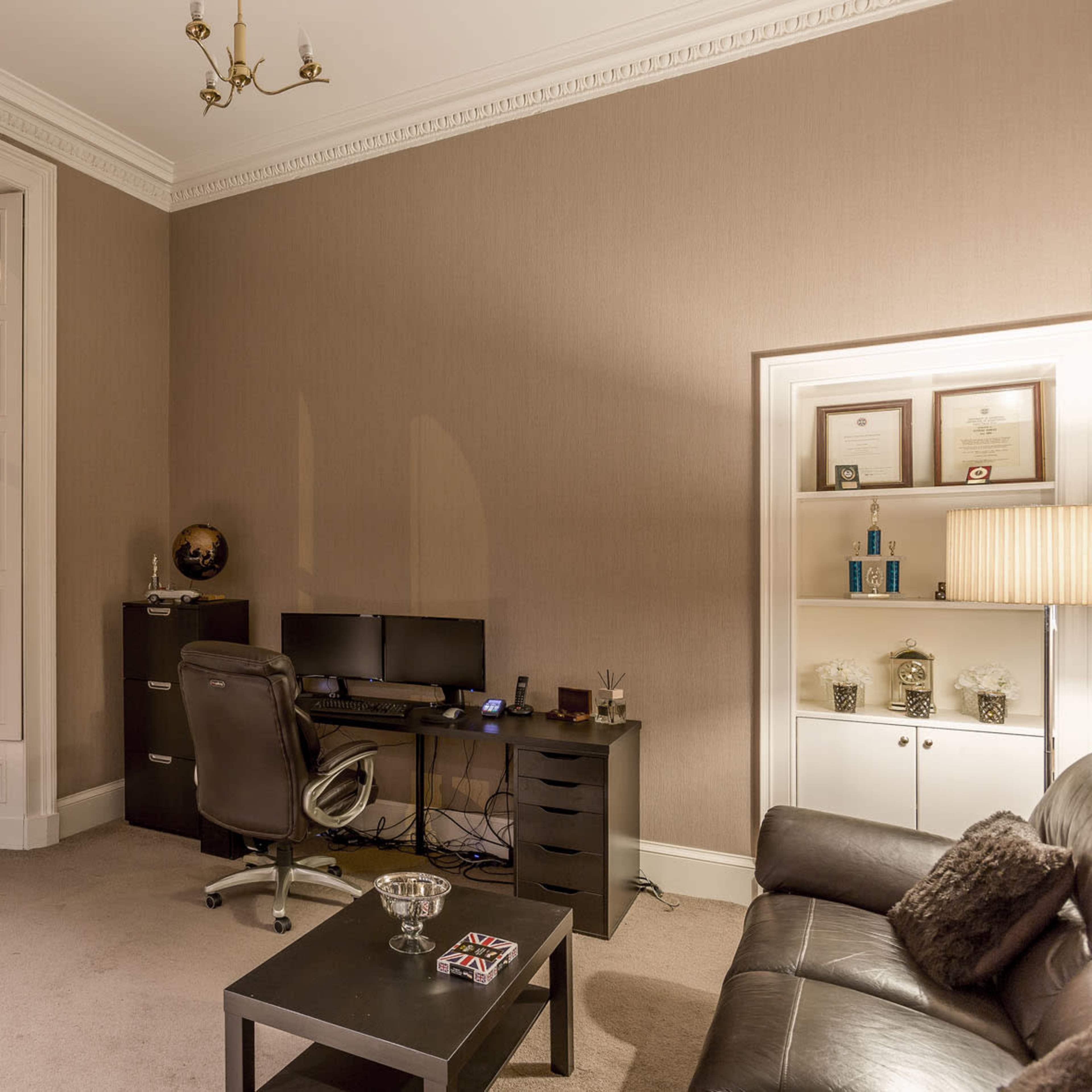 A modern office space with a desk and two monitors, a leather couch, and a large window overlooking a cityscape.