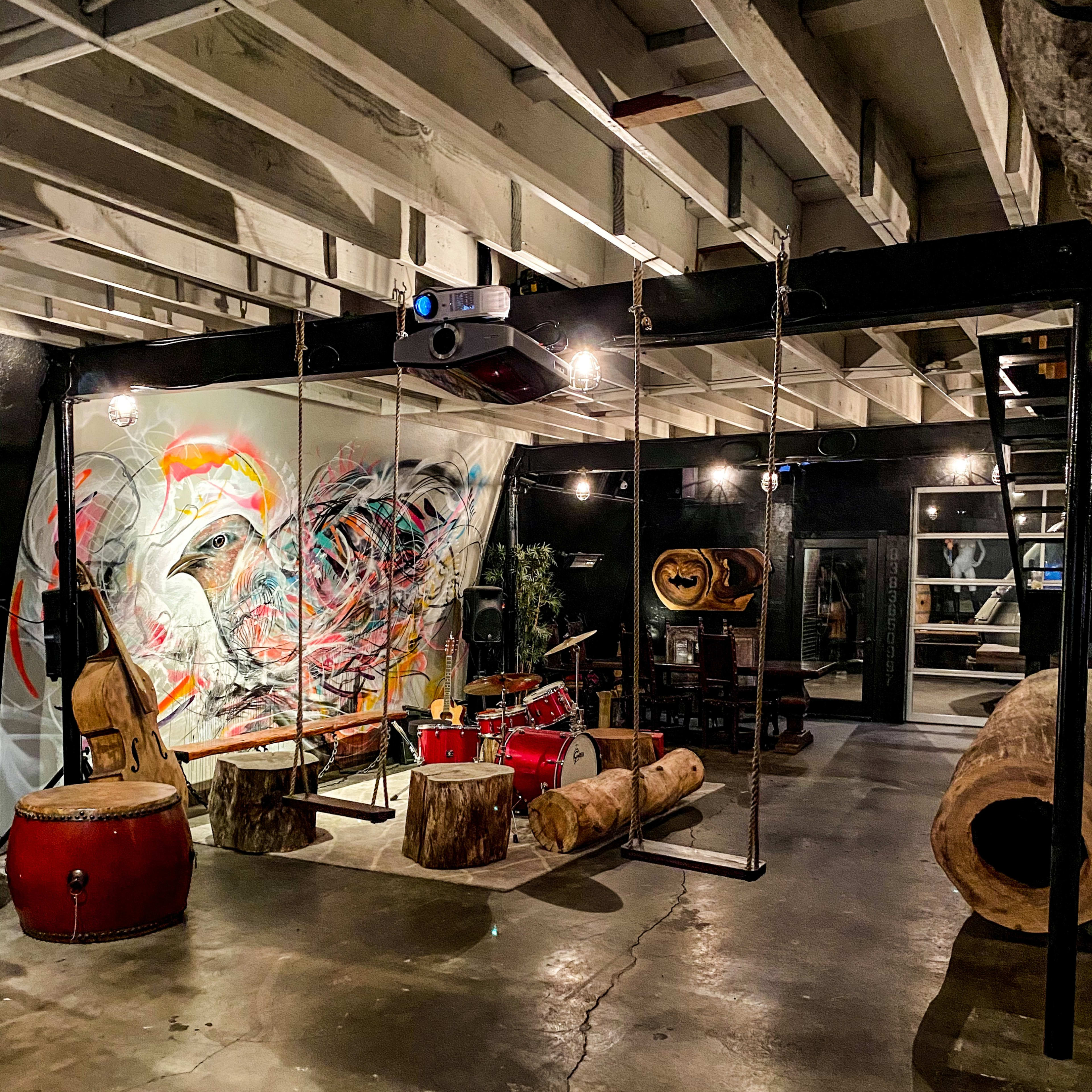 An industrial-style room with swings made from logs, a colorful mural on the wall, and musical instruments arranged in an artistic setup.
