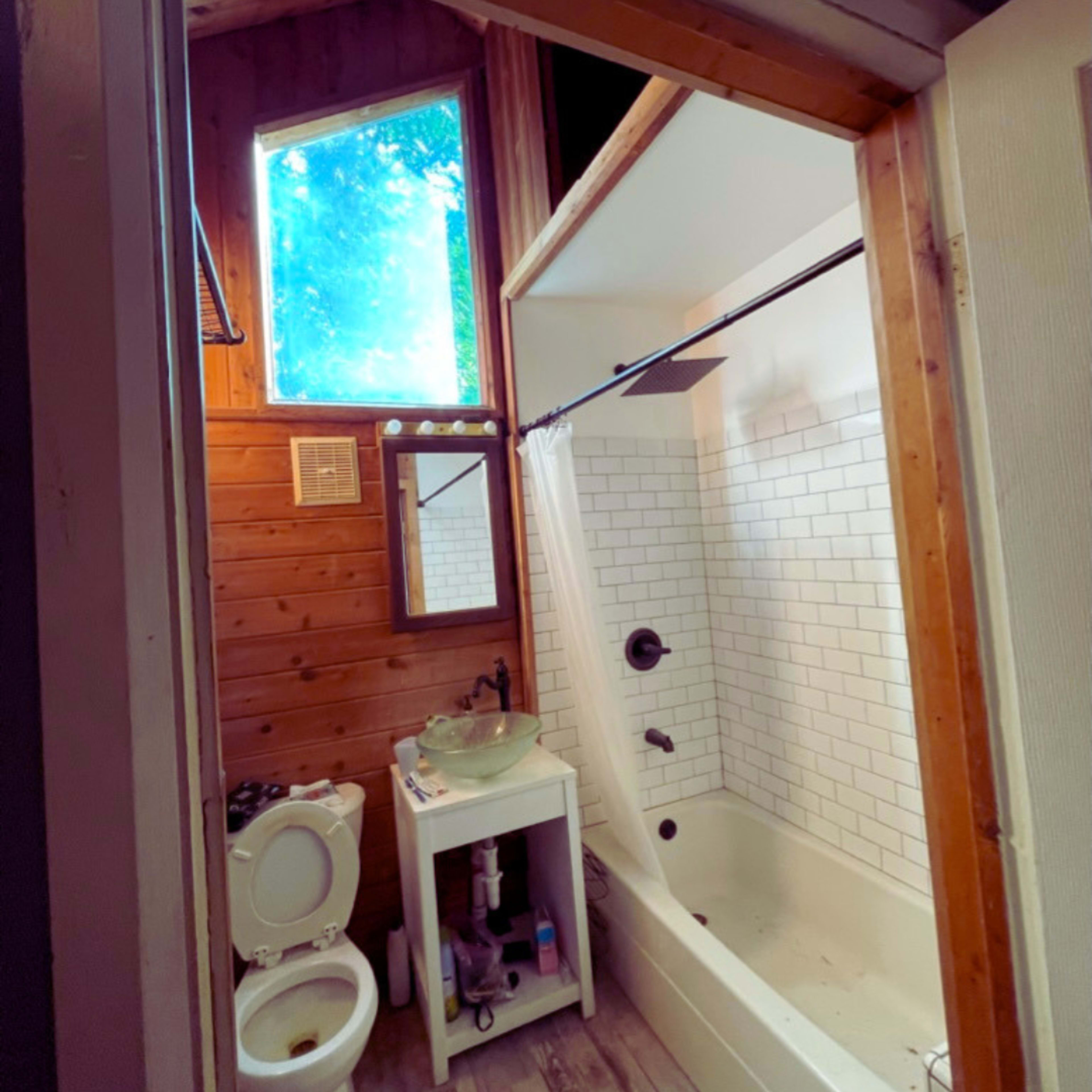 A bathroom with a bathtub, a toilet, a small sink on a stand, and a window allowing natural light.
