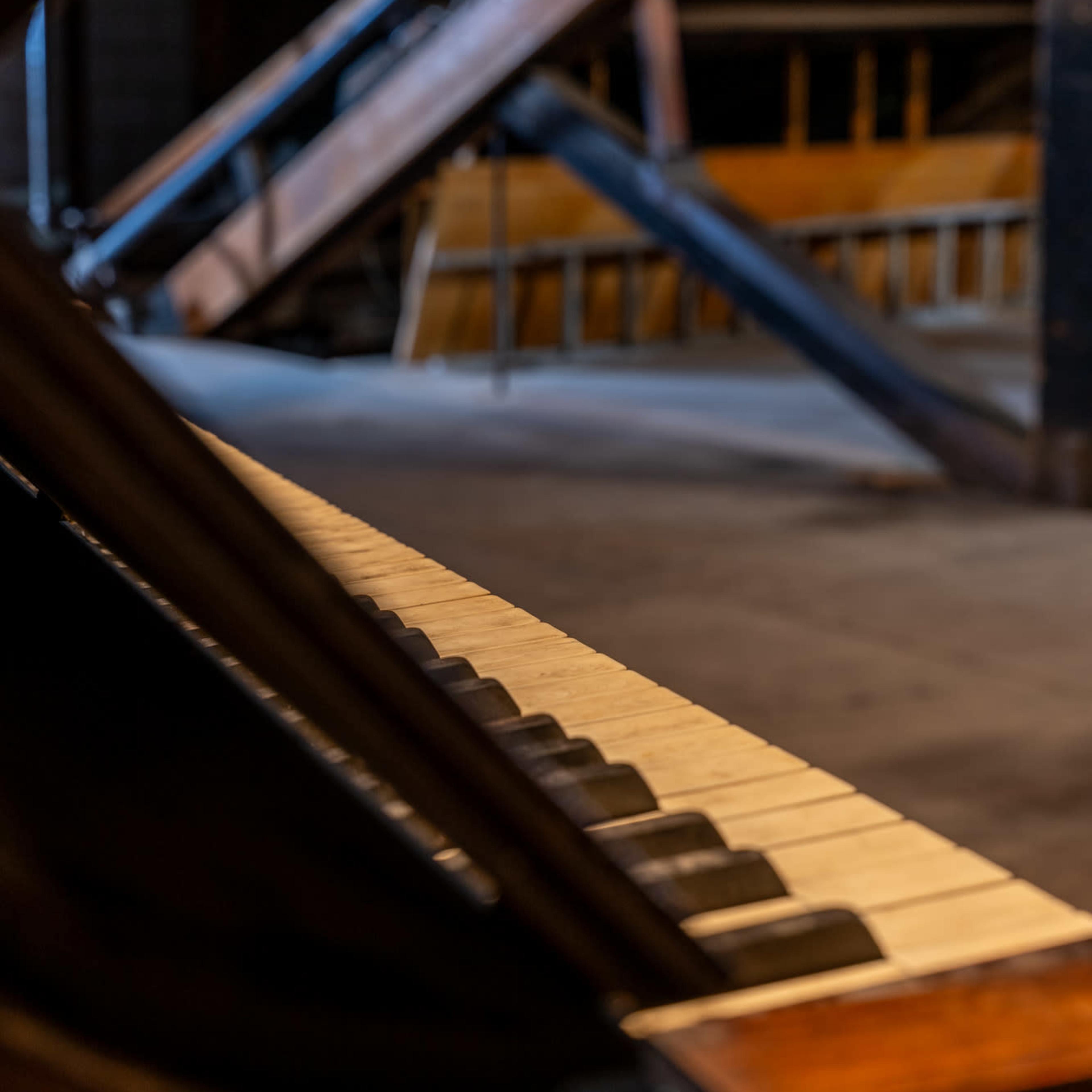 An old piano with a focus on its keys, set in an attic with wooden beams and a spacious floor visible in the background.