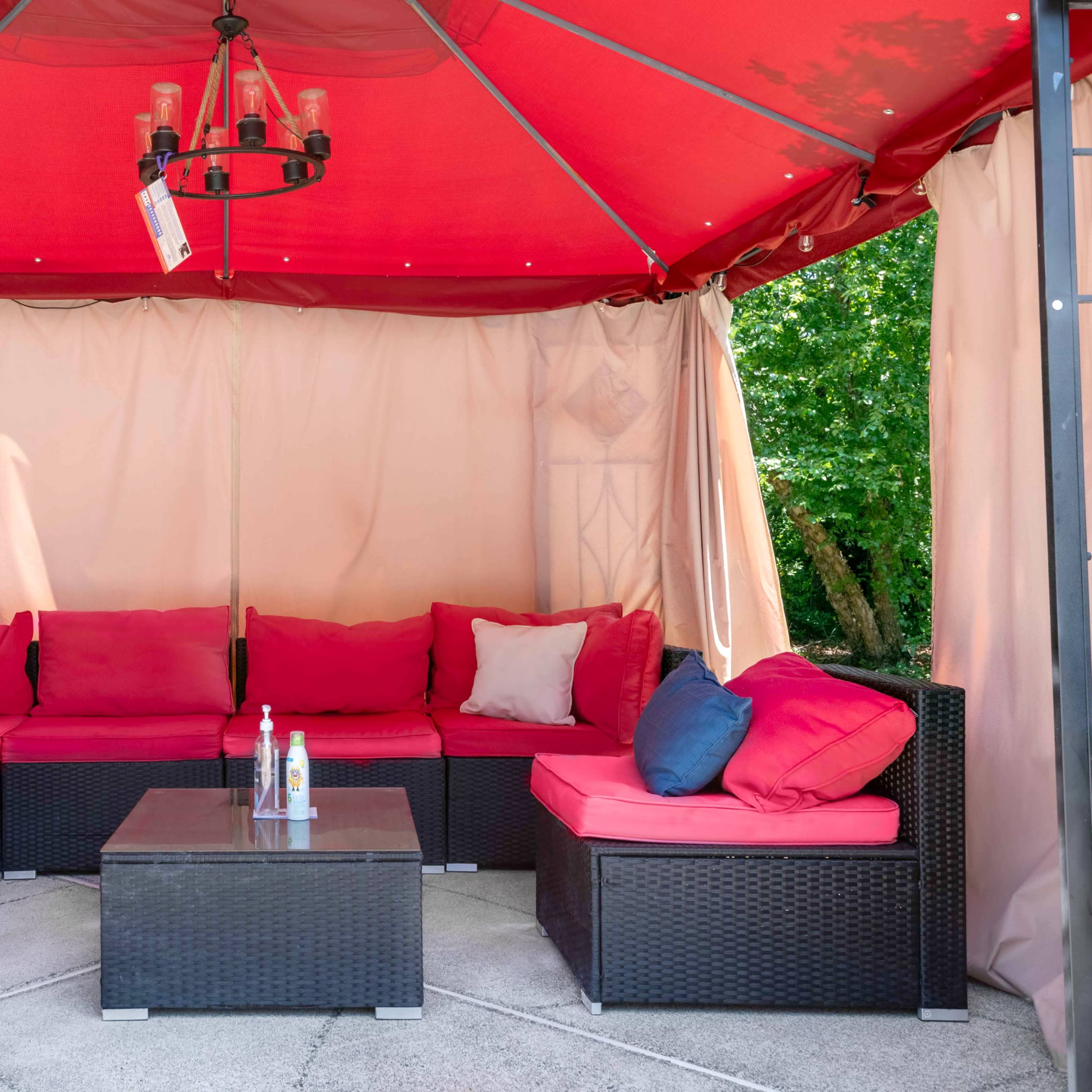 A covered outdoor seating area with a red canopy, brown wicker furniture, and a table in the center.