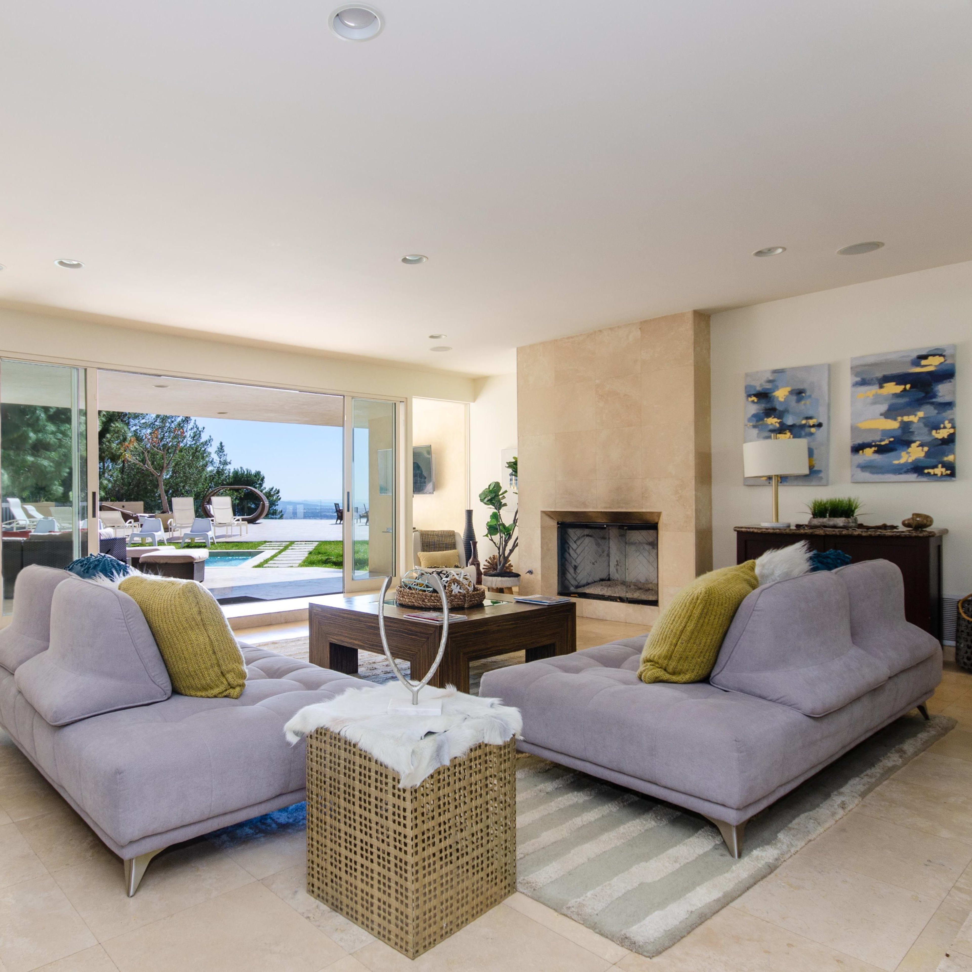 A modern living room with two gray sofas facing a coffee table, large glass doors leading to a patio, and a view of the outdoors.