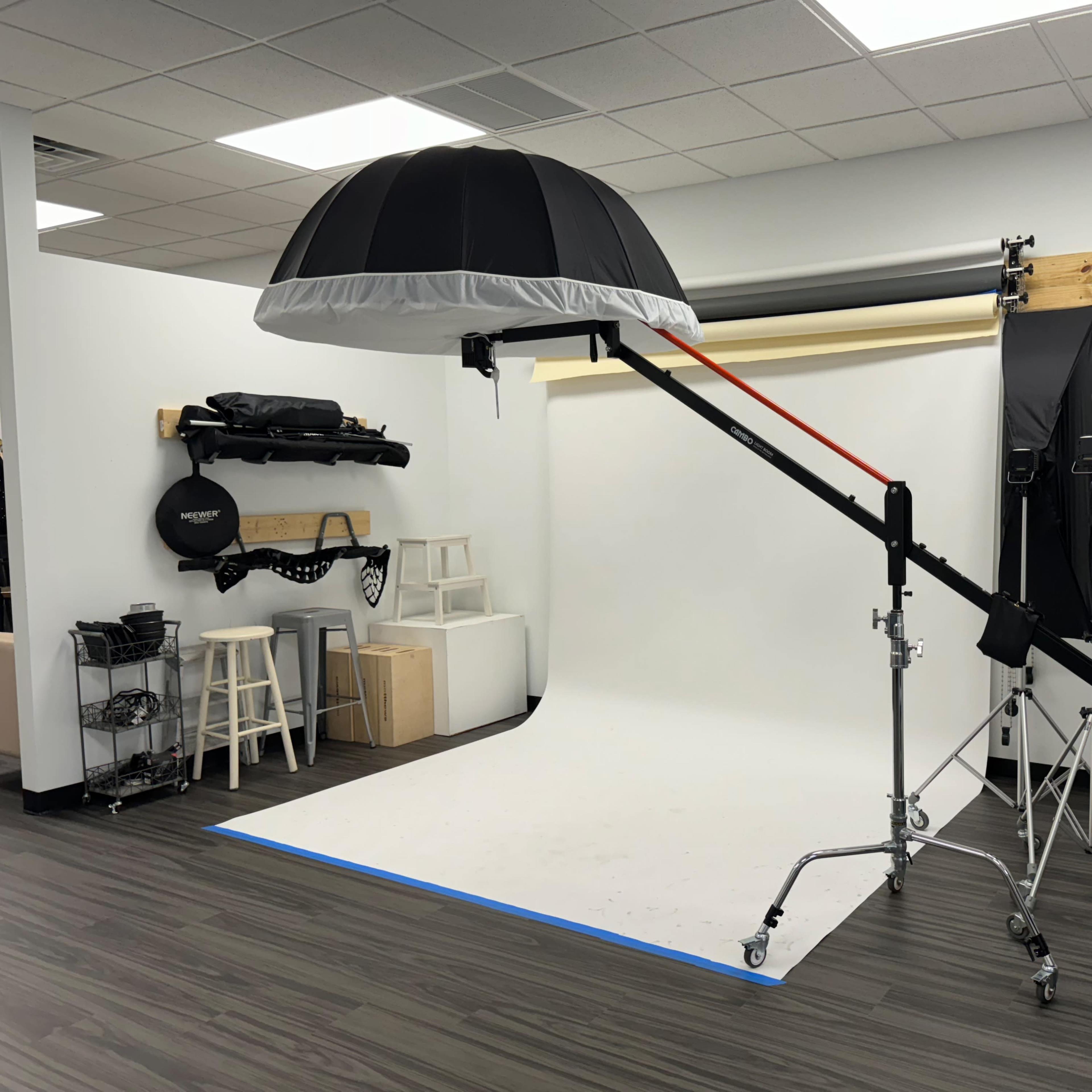 A photography studio setup with a backdrop, lighting equipment, and a large softbox attached to a boom arm.
