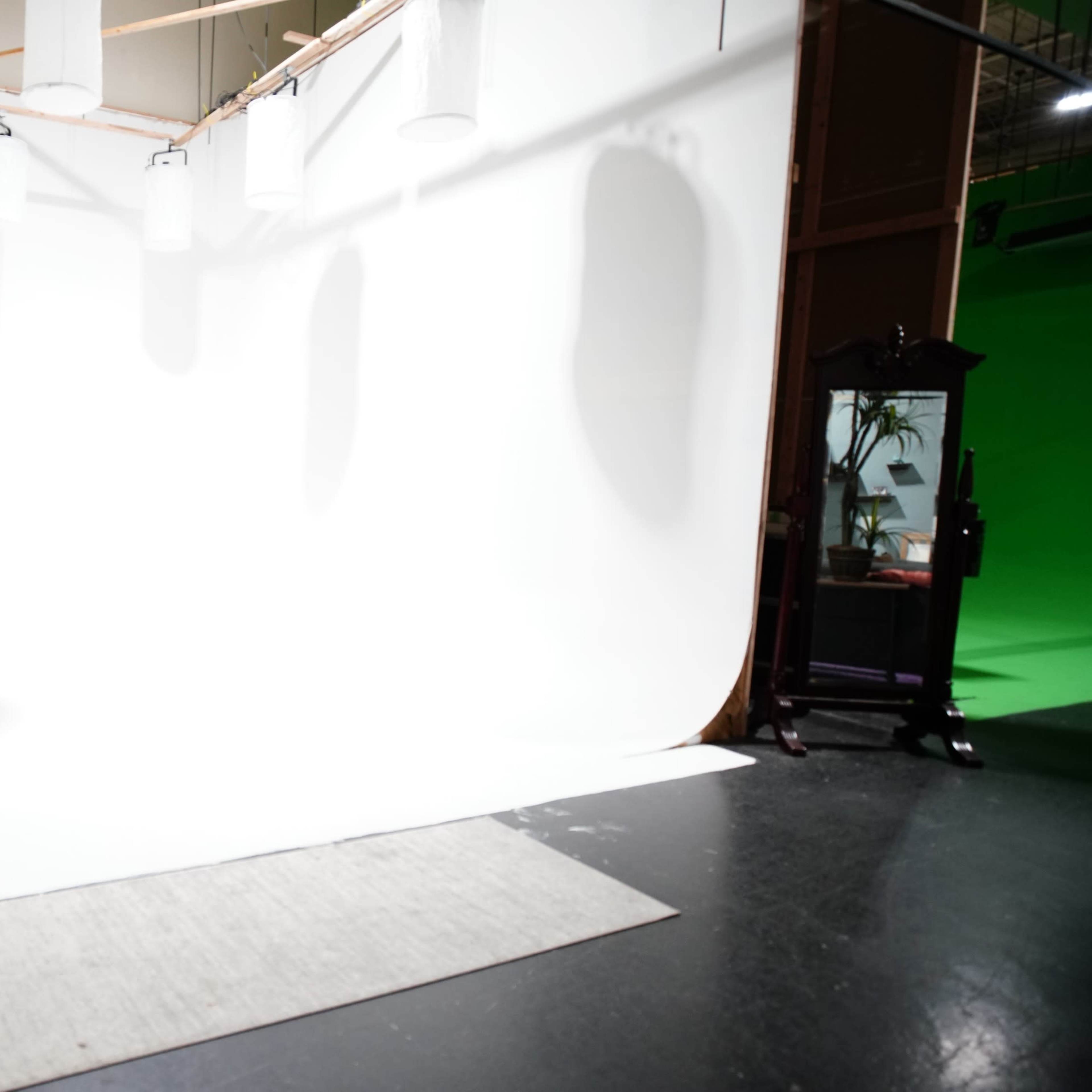 A photography studio with a white backdrop, spotlights, and a green screen on one side.