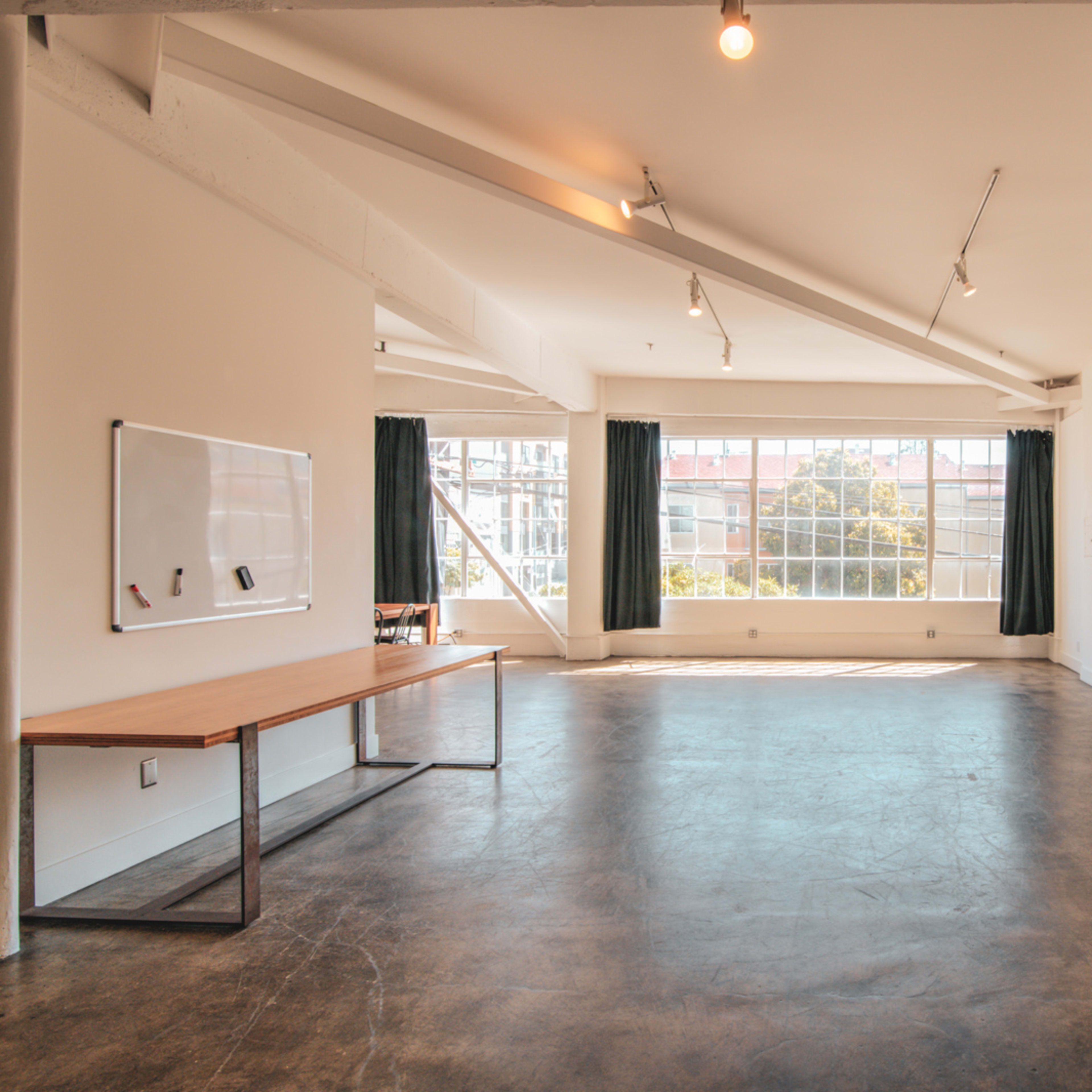 A spacious, modern room with large windows, a concrete floor, a wooden table, and minimalistic decor.