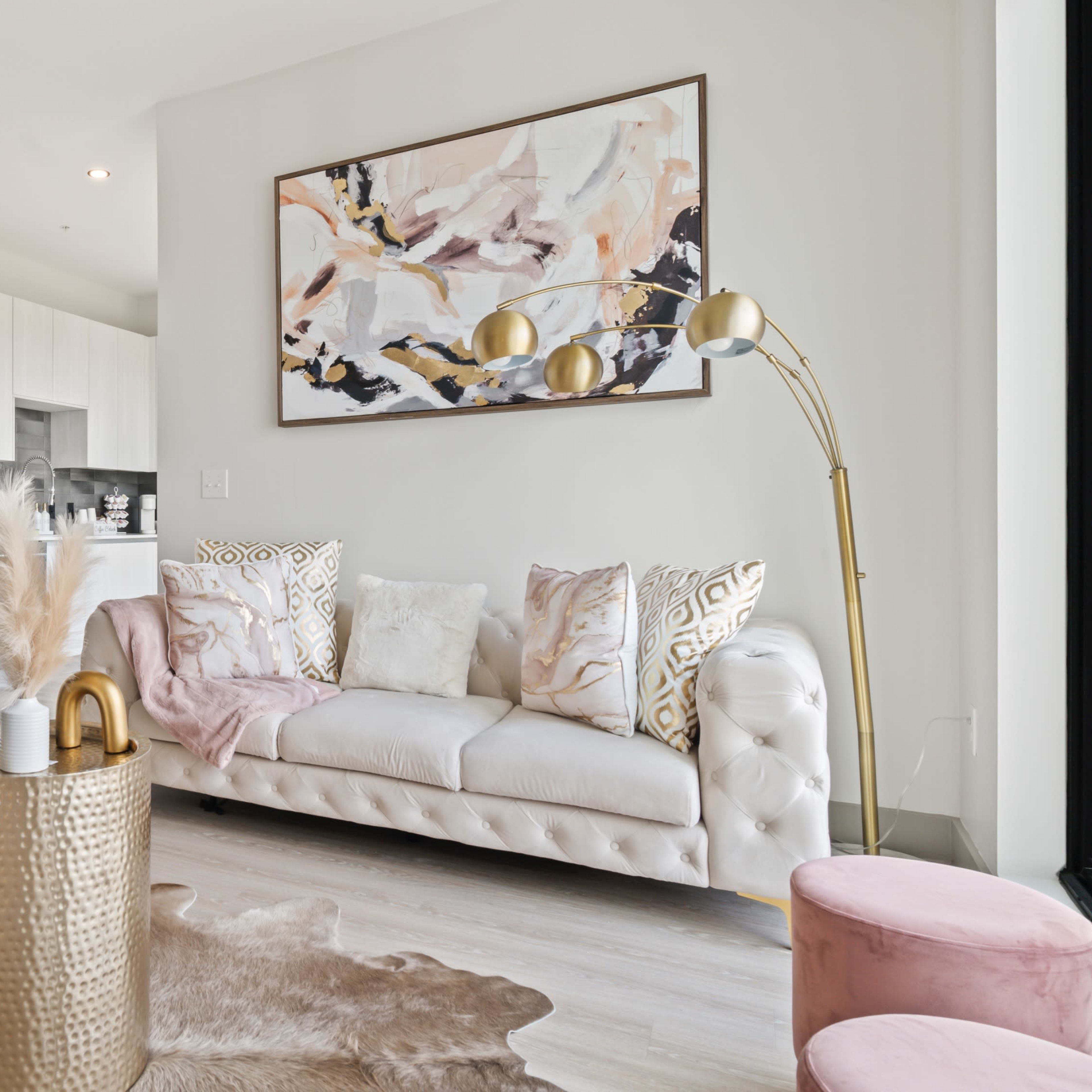 A modern living room features a beige sofa, gold accents, and a decorative area rug, with an open kitchen visible in the background.