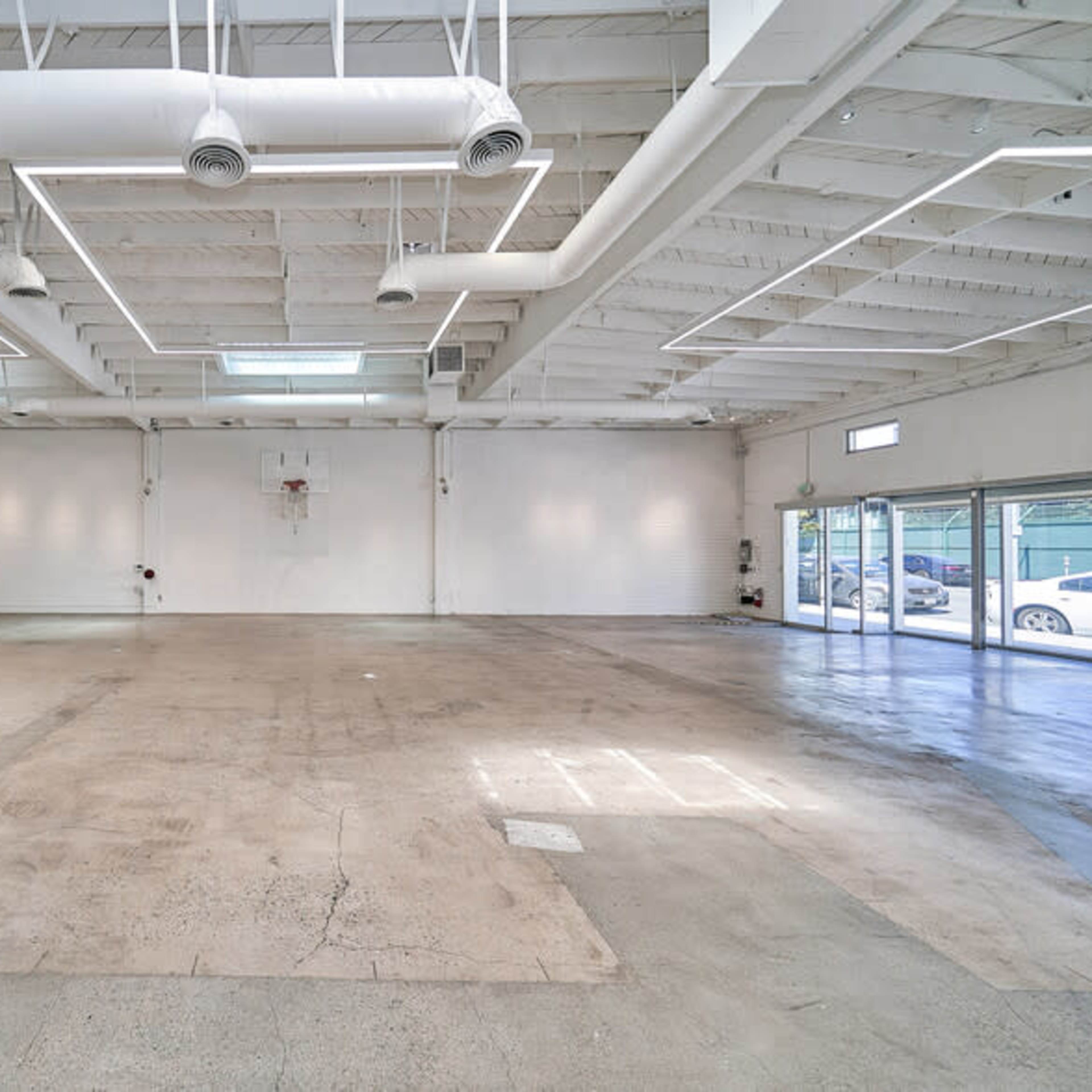 A spacious, empty interior of a commercial building with high ceilings, large windows, and a smooth concrete floor.