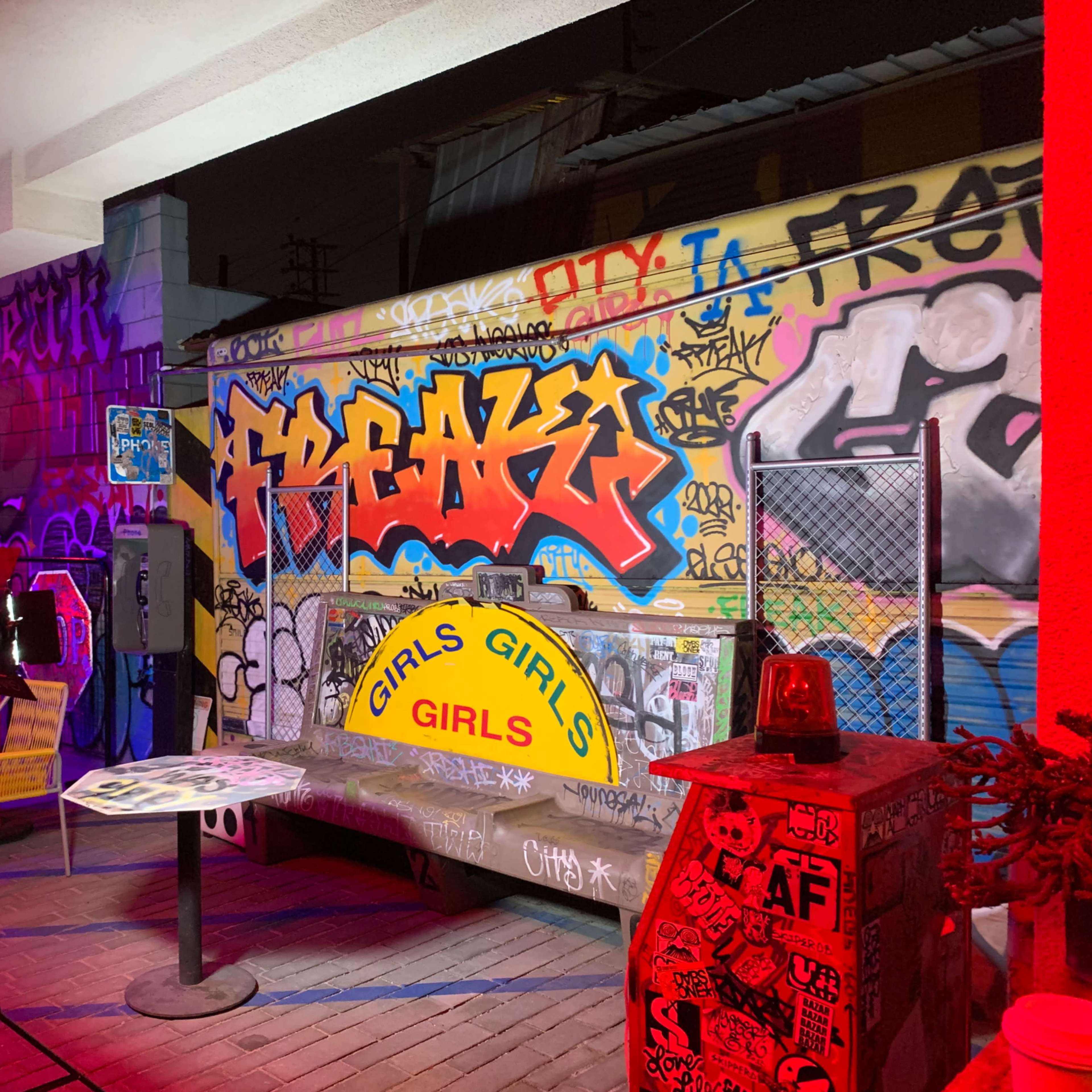 The scene shows a graffiti-covered outdoor area with a table and a sign that reads "GIRLS GIRLS GIRLS."